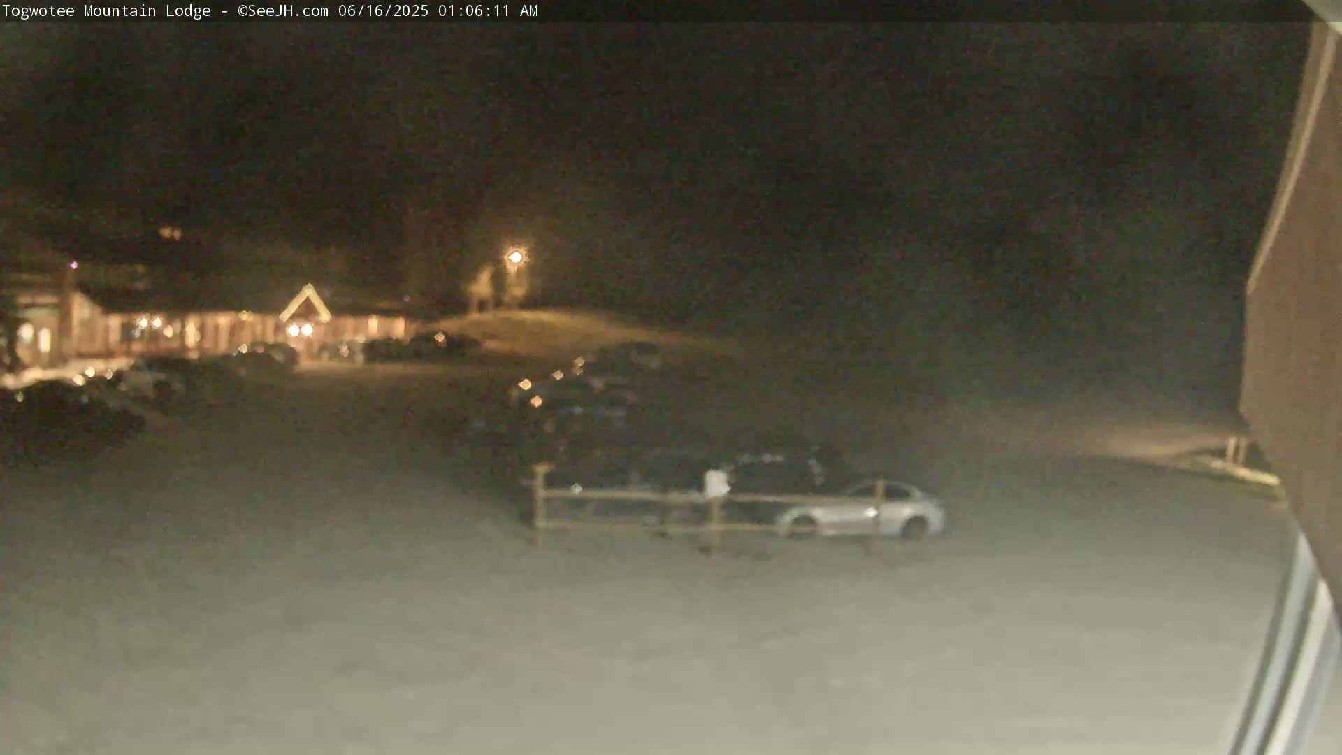 A nighttime view of a lodge with a parking lot containing several cars, under dark and unclear weather conditions.
