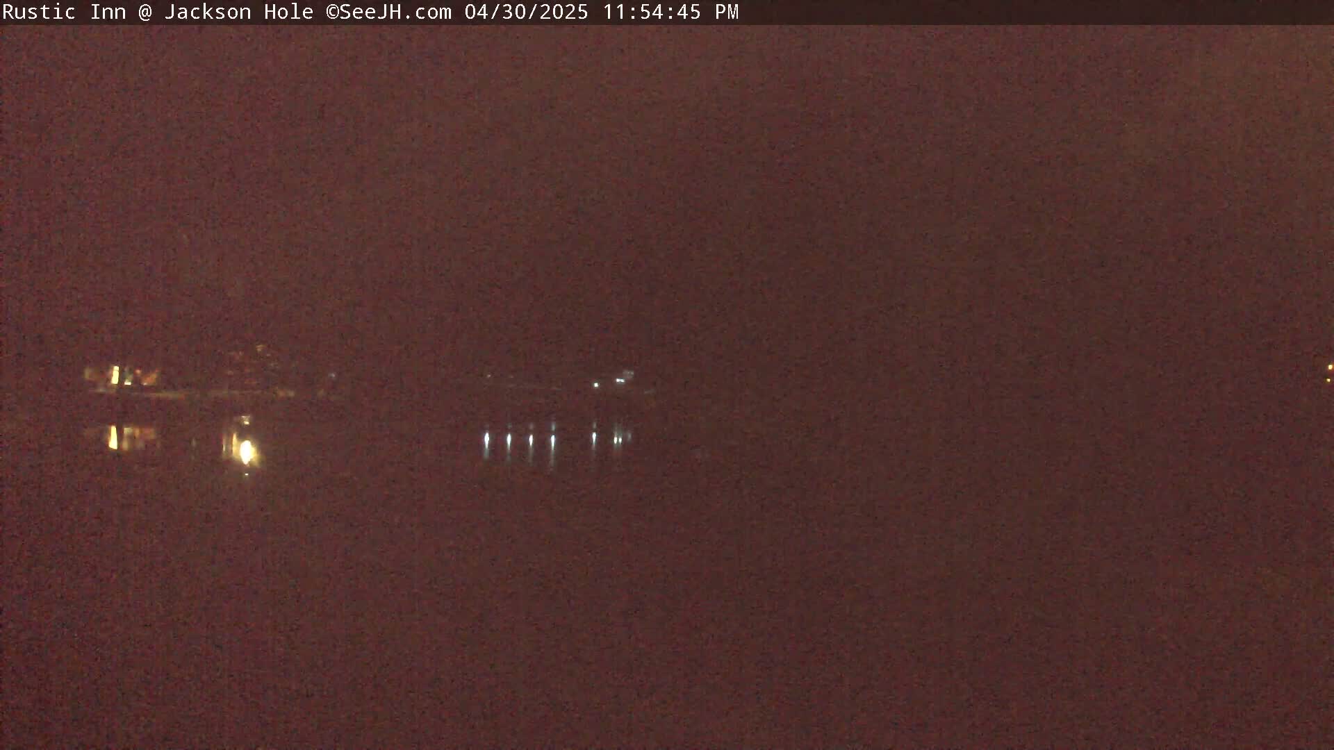 A dark, nighttime scene shows a body of water reflecting a few lights from across the shore.