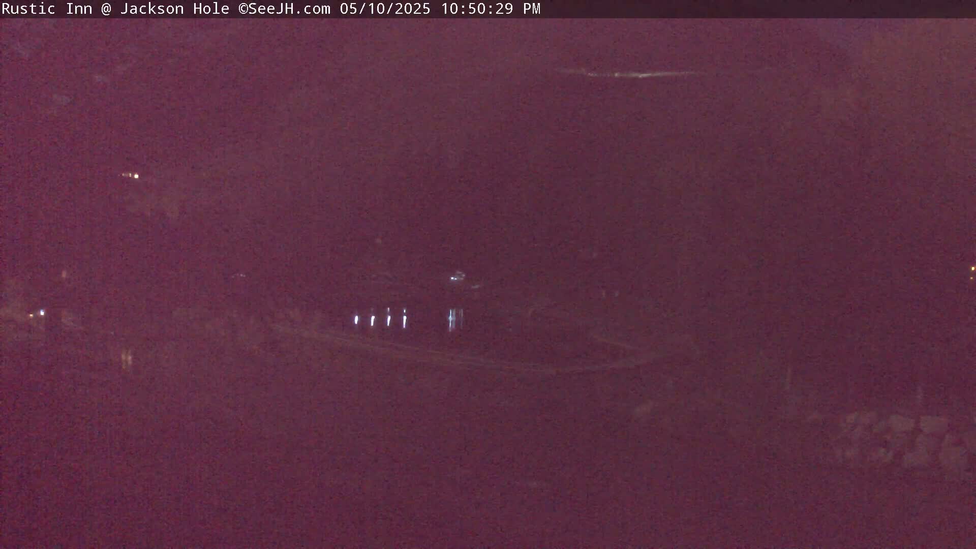 A nighttime, low-light view shows a dark landscape with a few faint lights and a body of water.