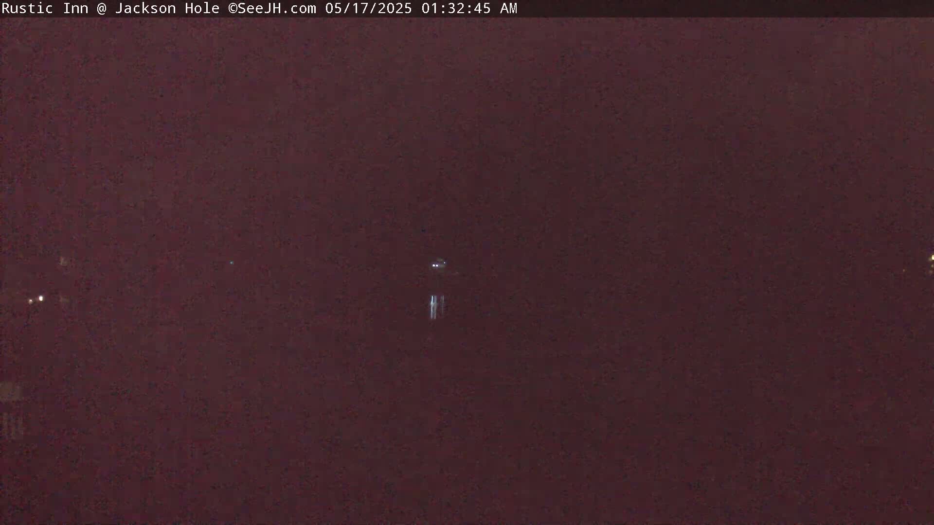 A dark, nighttime scene shows a few faint lights in the distance under a mostly clear sky.