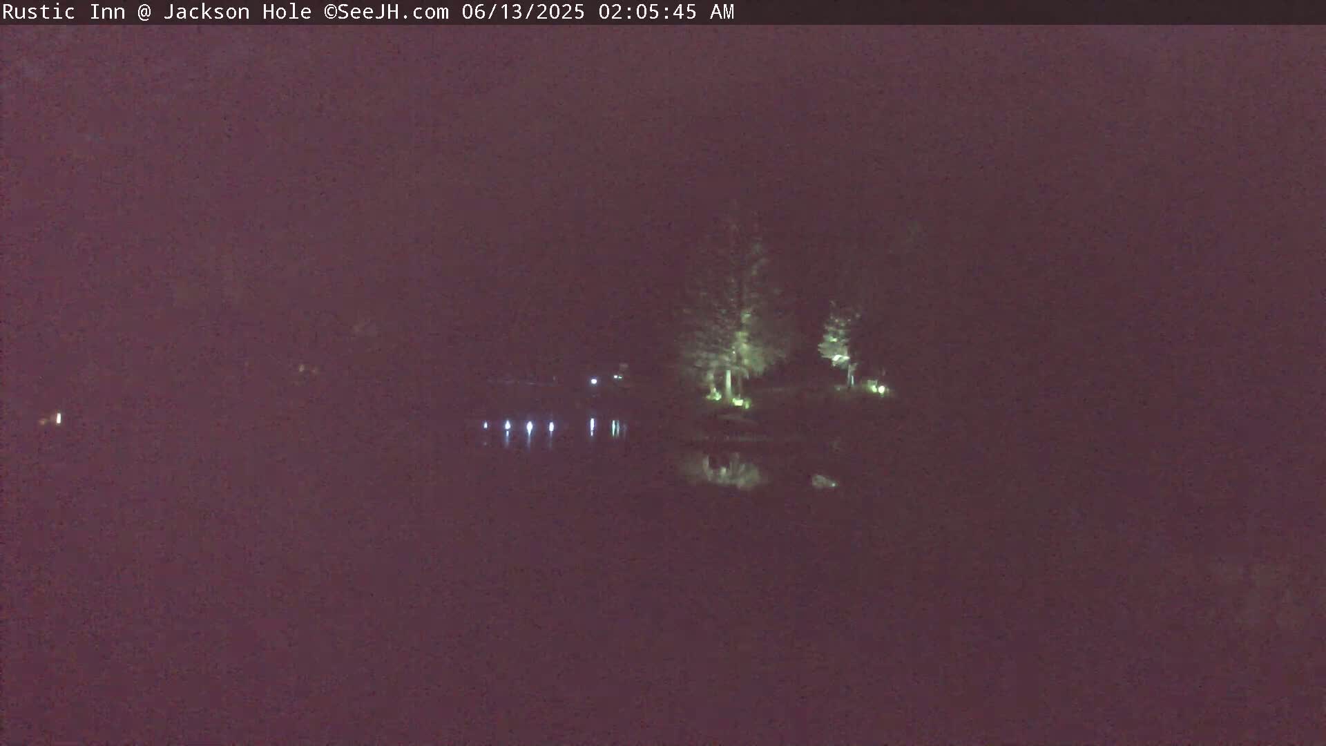 A nighttime view of a calm body of water reflecting illuminated trees and lights on the far shore under a dark sky.