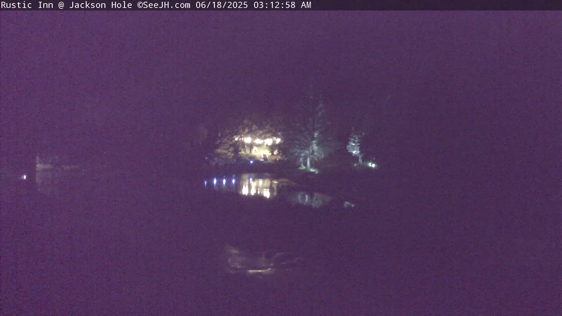 A nighttime view shows a body of water reflecting the lights of a building nestled among trees.