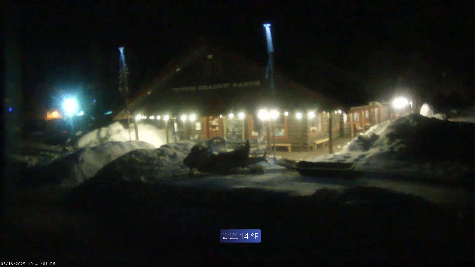 A snow-covered, illuminated building at night with a snowmobile parked in front, the temperature is 14°F.