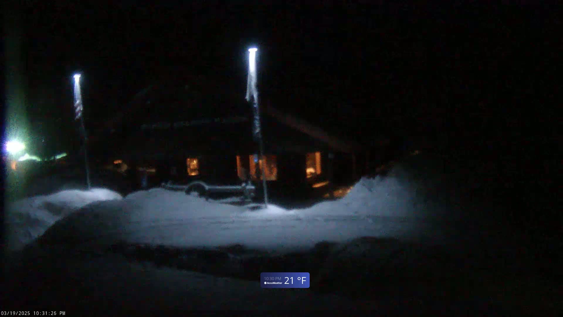 At night in snowy conditions, illuminated light posts stand near a dark building with lit windows.
