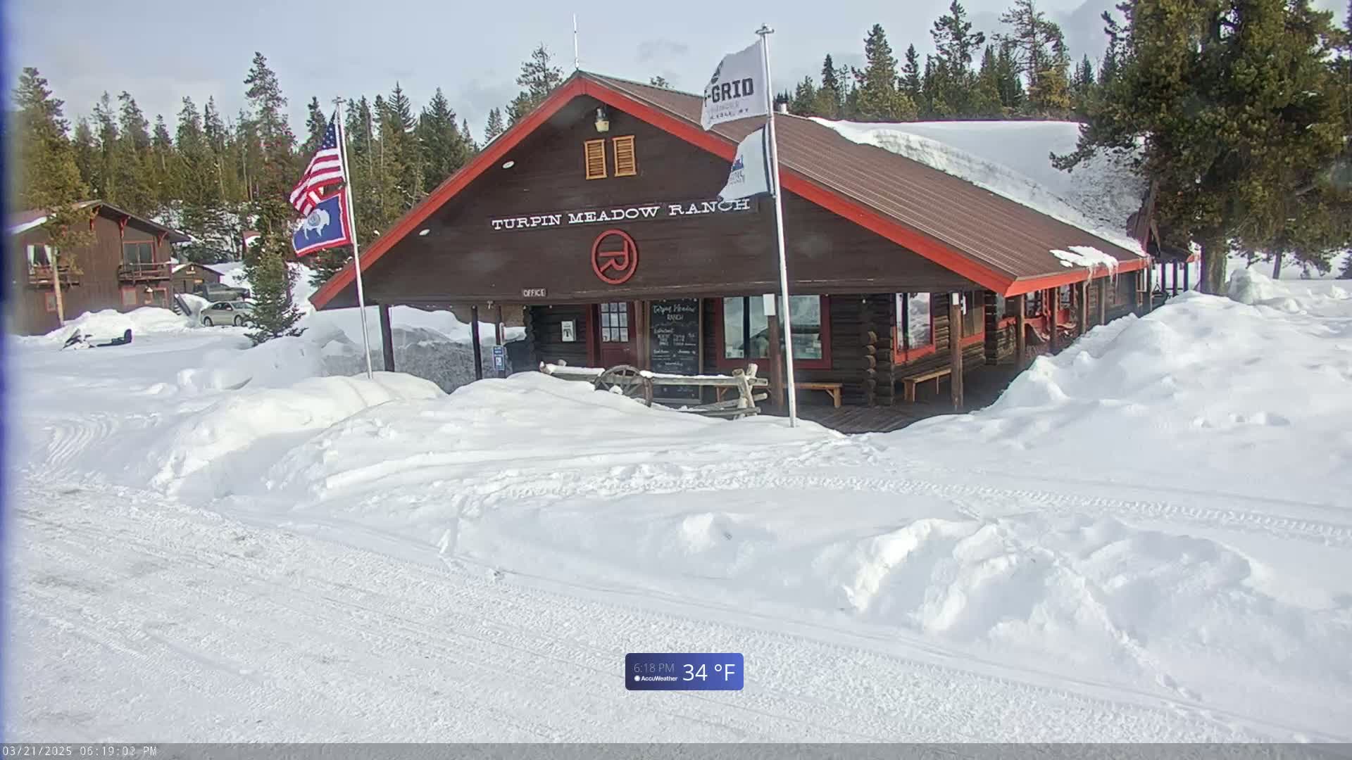 A brown log cabin with a red roof, labeled "Turpin Meadow Ranch," sits in a snowy landscape under a bright, sunny sky.