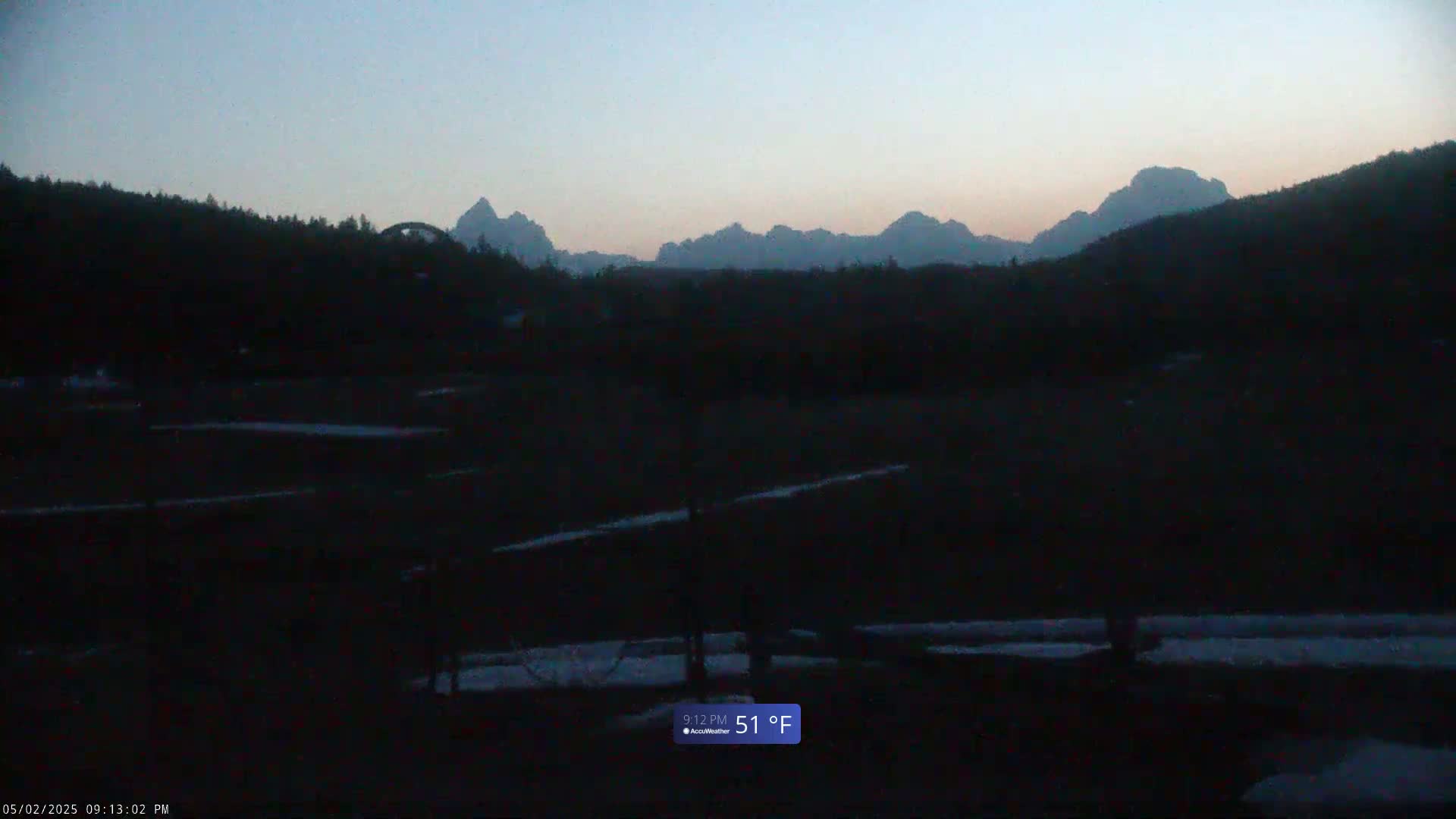 A dark, mountainous landscape at twilight, with patches of snow on the ground, and a temperature of 51°F.