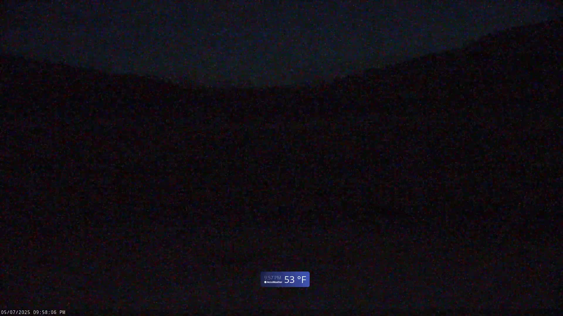 A dark, nighttime view of a hilly landscape under a clear sky, with a temperature of 53 degrees Fahrenheit.