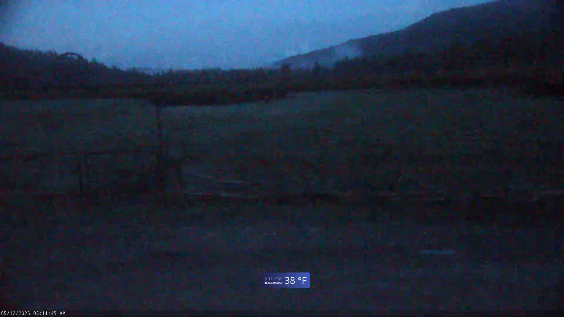 A dark, flat field is visible under a twilight sky, with a hill in the background, in 38-degree weather.