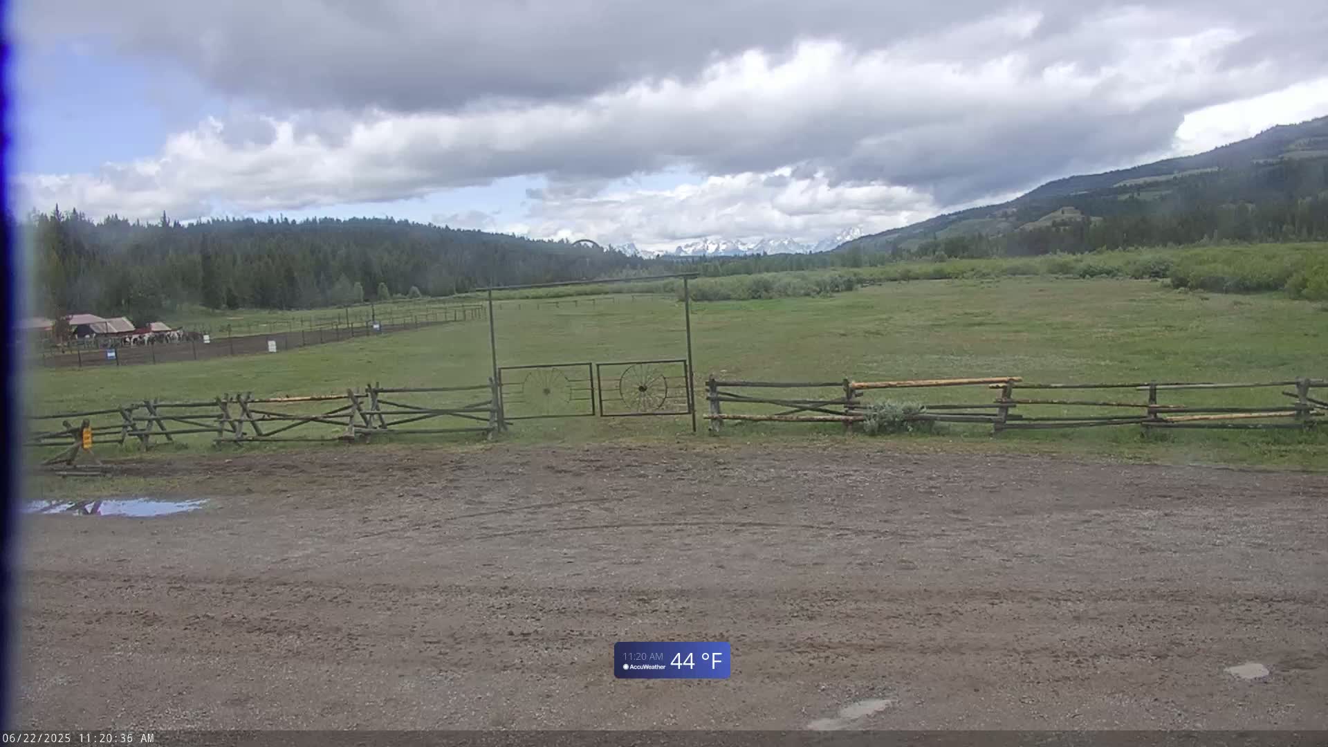 A grassy field with a wooden fence and gate, under a cloudy sky, and mountains in the background.