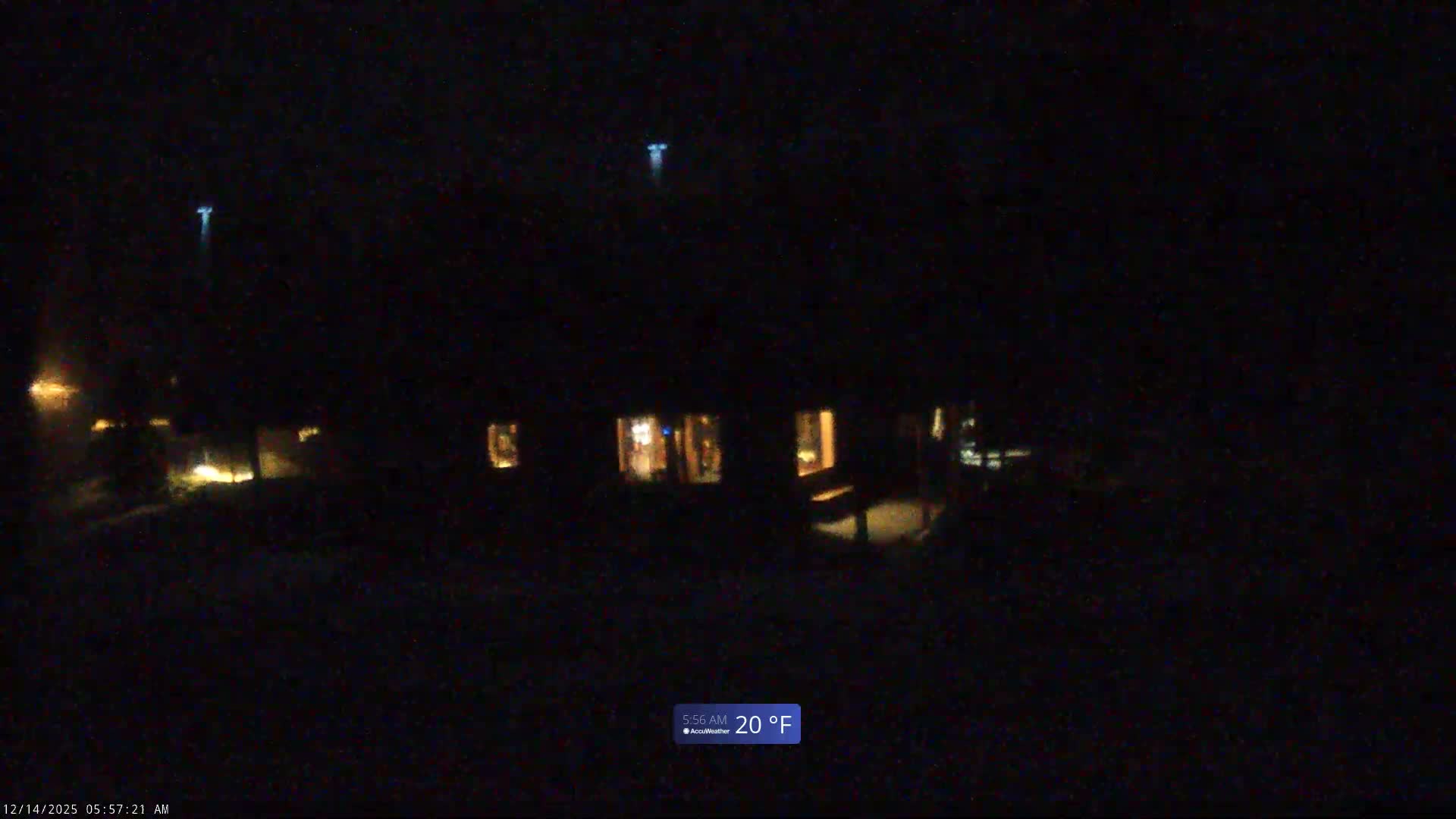 A dark, grainy image captures a snow-covered outdoor landscape at night, featuring a fence in the foreground and dark, distant hills under a hazy sky, indicating cold winter weather.