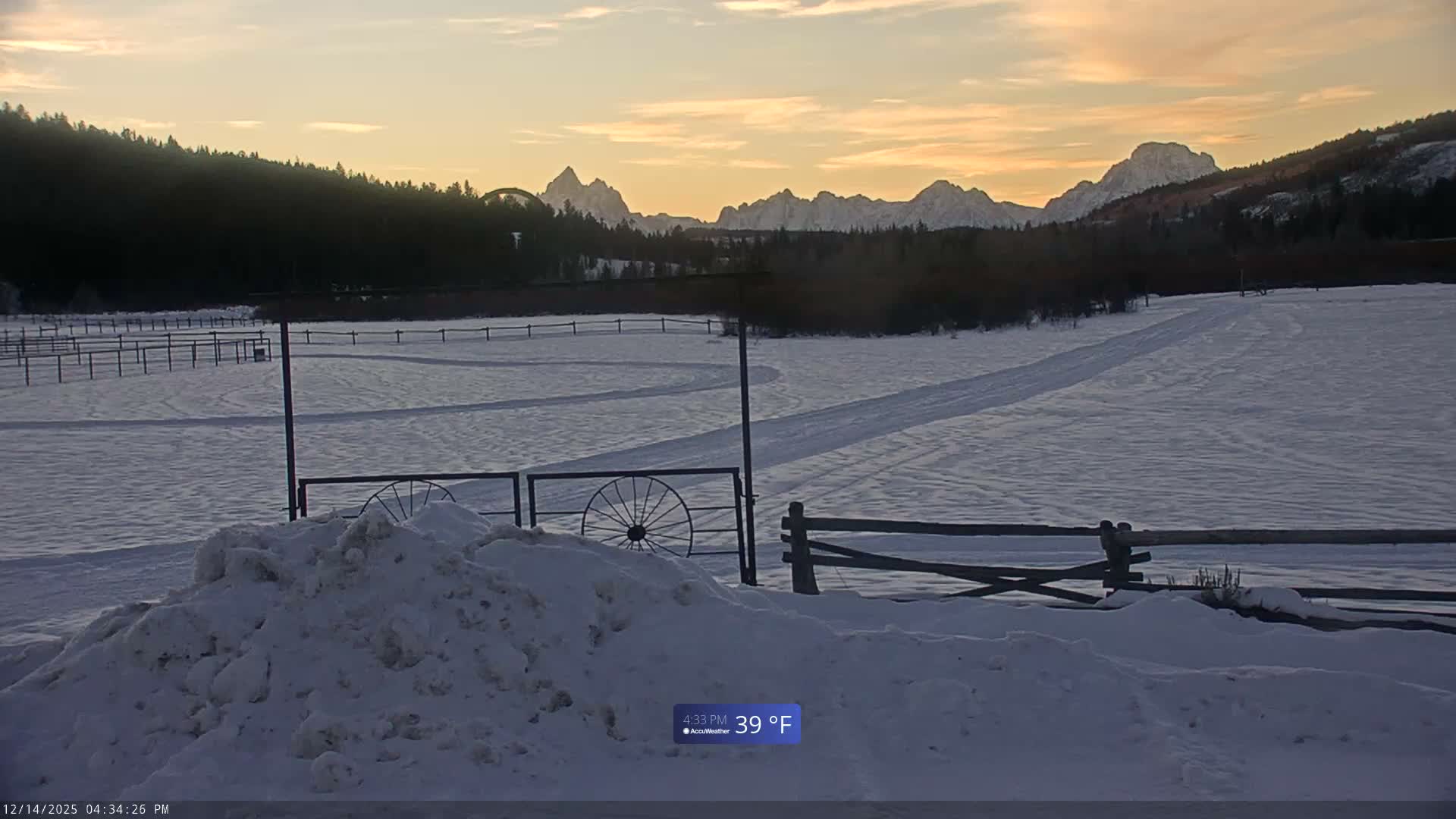 A dark, grainy image captures a snow-covered outdoor landscape at night, featuring a fence in the foreground and dark, distant hills under a hazy sky, indicating cold winter weather.