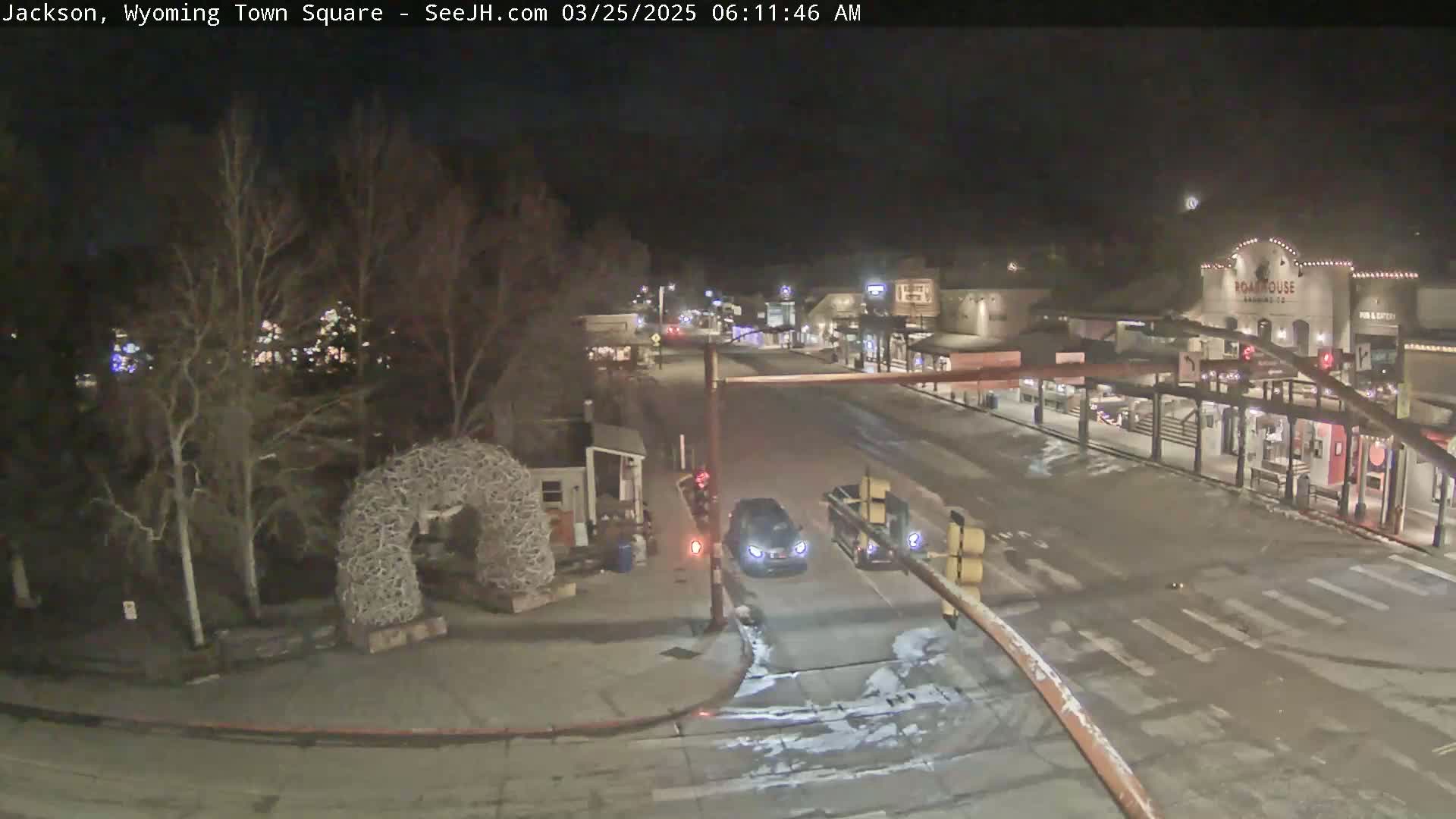 A nighttime view of a town square with a few cars and light snow on the ground.