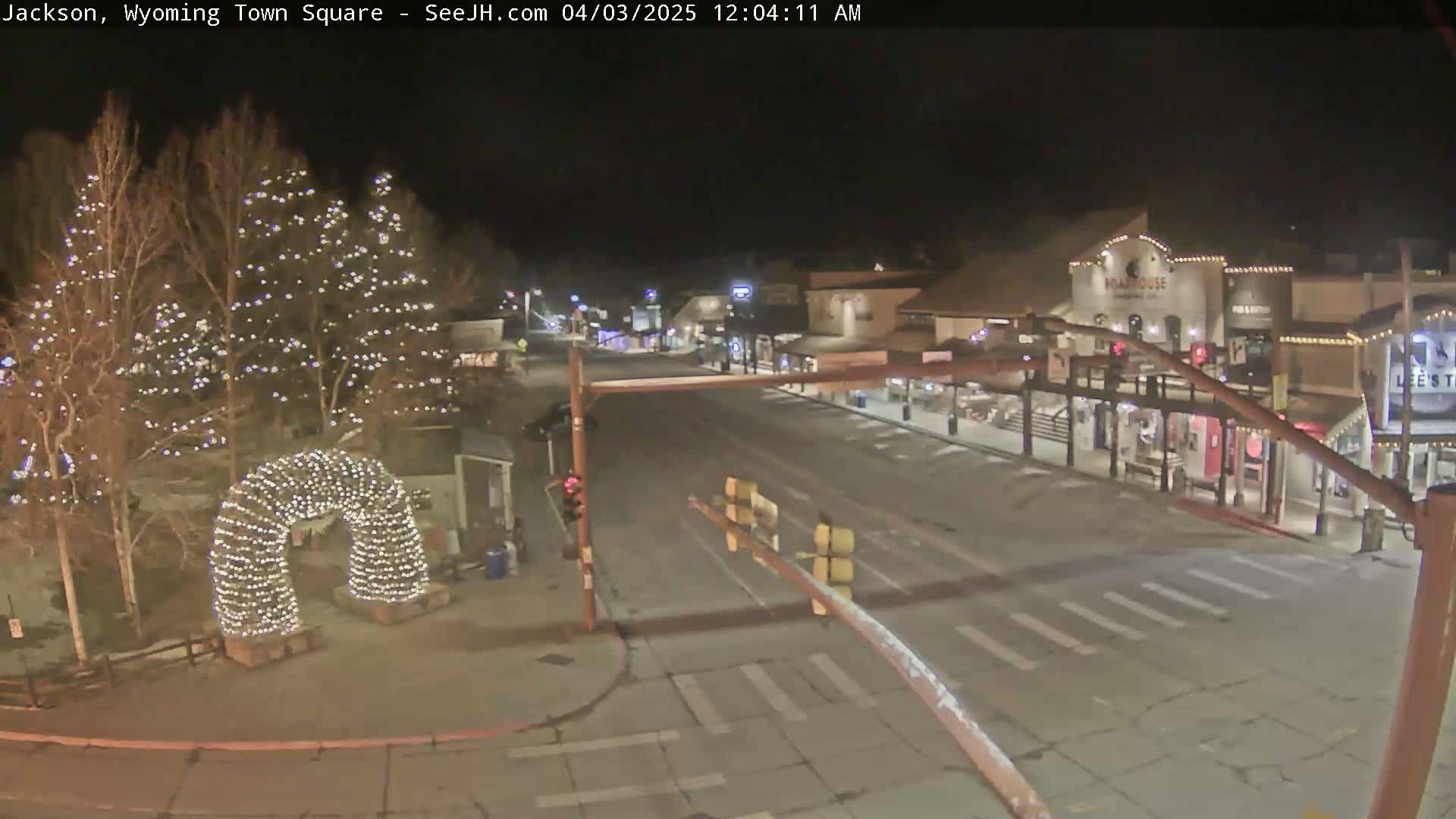 A nighttime view of a town square, featuring a street with crosswalks, buildings with lights, and a lighted archway in the foreground under a clear sky.
