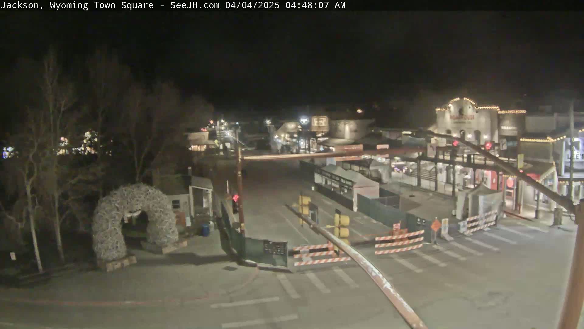 A nighttime view of a town square with some buildings, a road, and construction barriers.