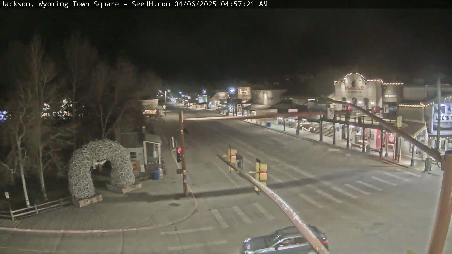 A mostly empty town square at night, with a few vehicles, is seen under dark, clear skies.