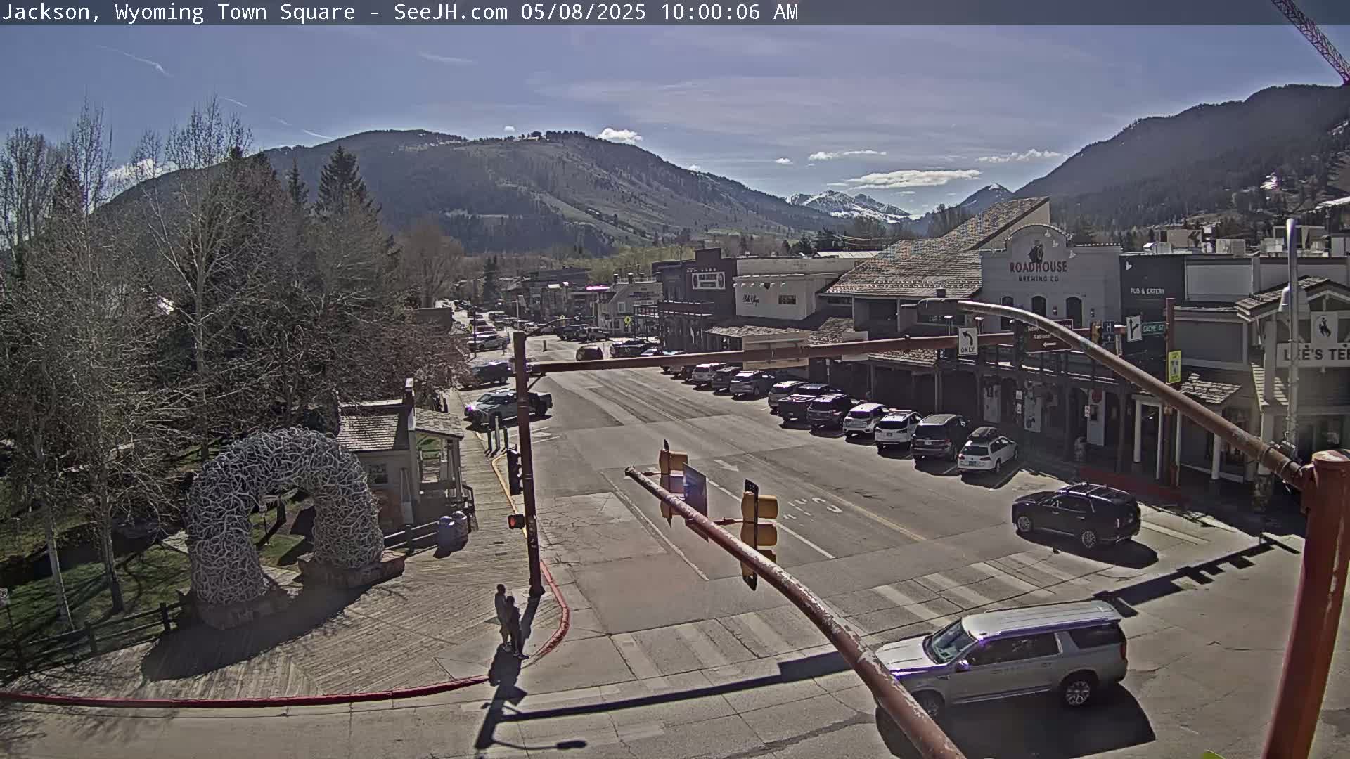 A sunny day reveals a town square with parked cars lining the streets, buildings with various storefronts, and a large antler archway.