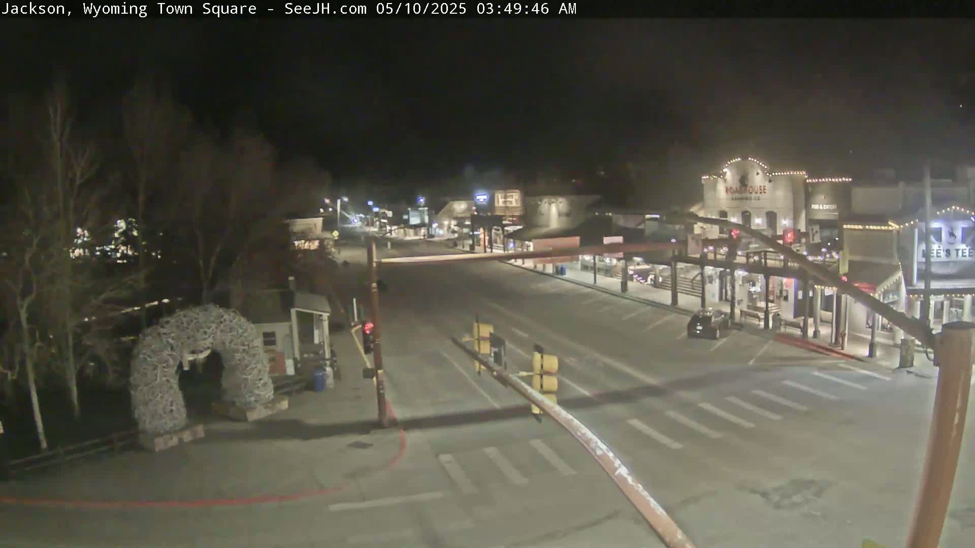 A mostly empty town square at night, with a few cars and buildings visible under dark skies.