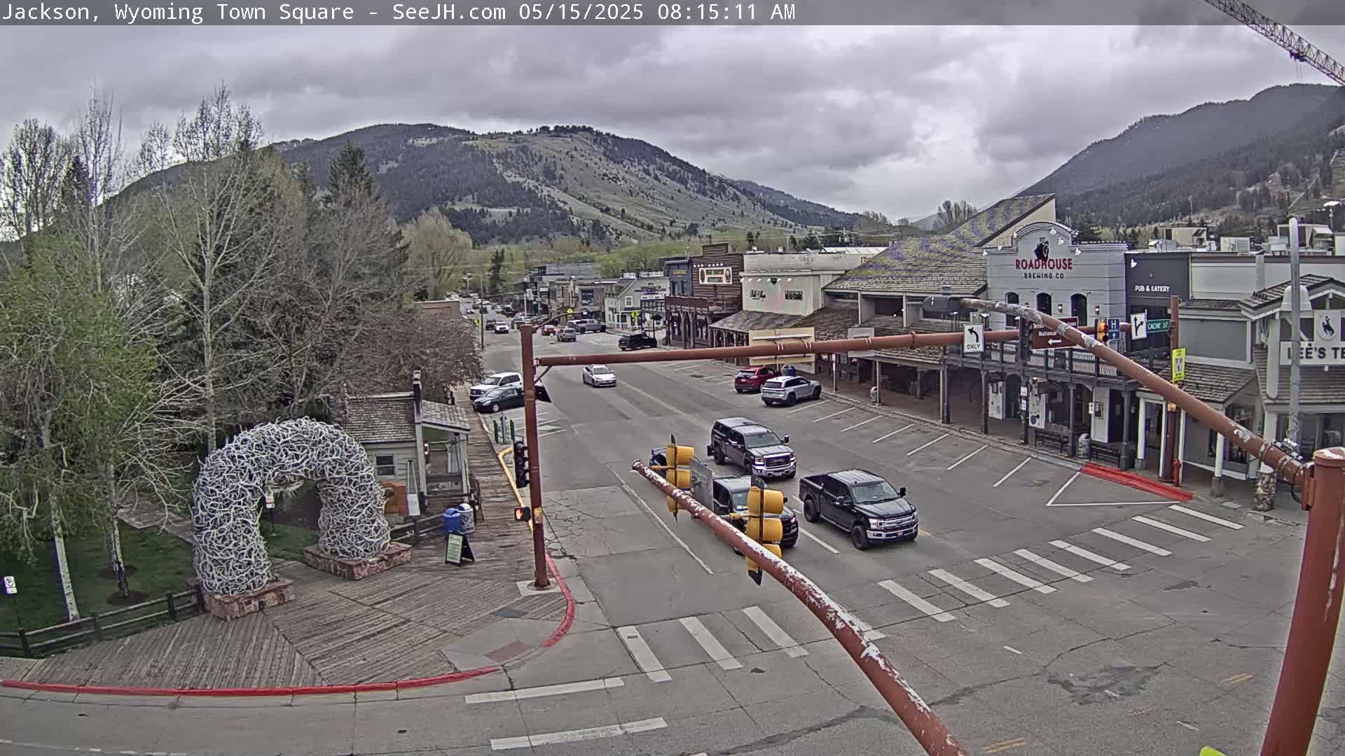 A town square with overcast skies, several vehicles at an intersection, and mountains in the background.