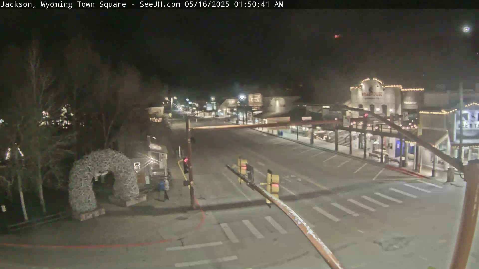A nighttime, empty town square with a few buildings visible and a large antler arch in the foreground under a clear sky.