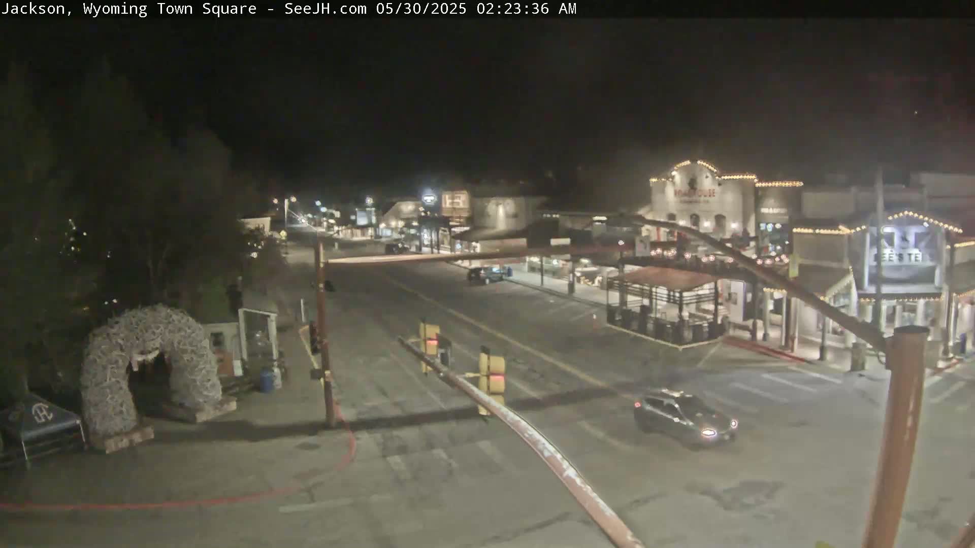 A nighttime, mostly empty town square with a few cars and buildings illuminated with lights.