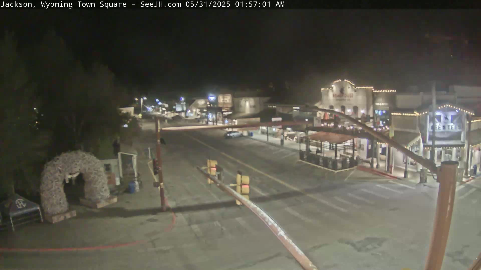 A nighttime view of a mostly empty town square with a few cars and buildings illuminated.