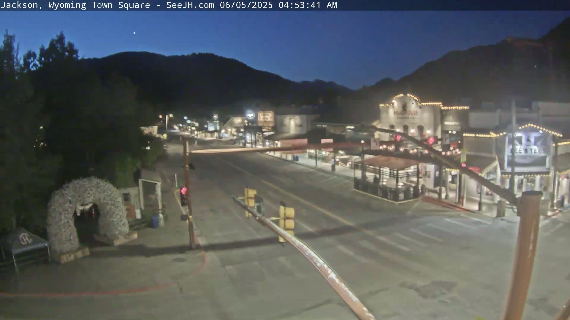 A mostly empty town square at night, under a dark blue twilight sky, with buildings and a few streetlights visible.