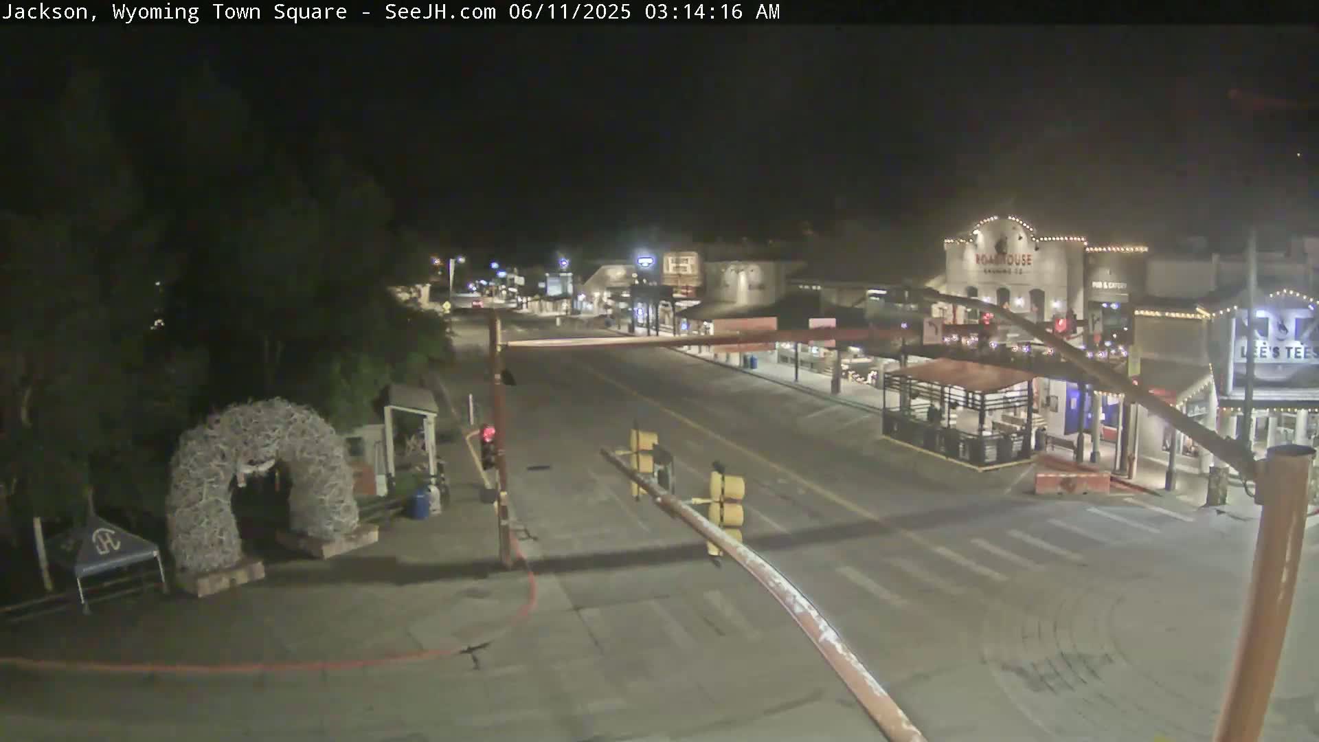 A mostly empty town square at night, under clear skies, with a few buildings visible and an archway made of what appears to be antlers in the foreground.