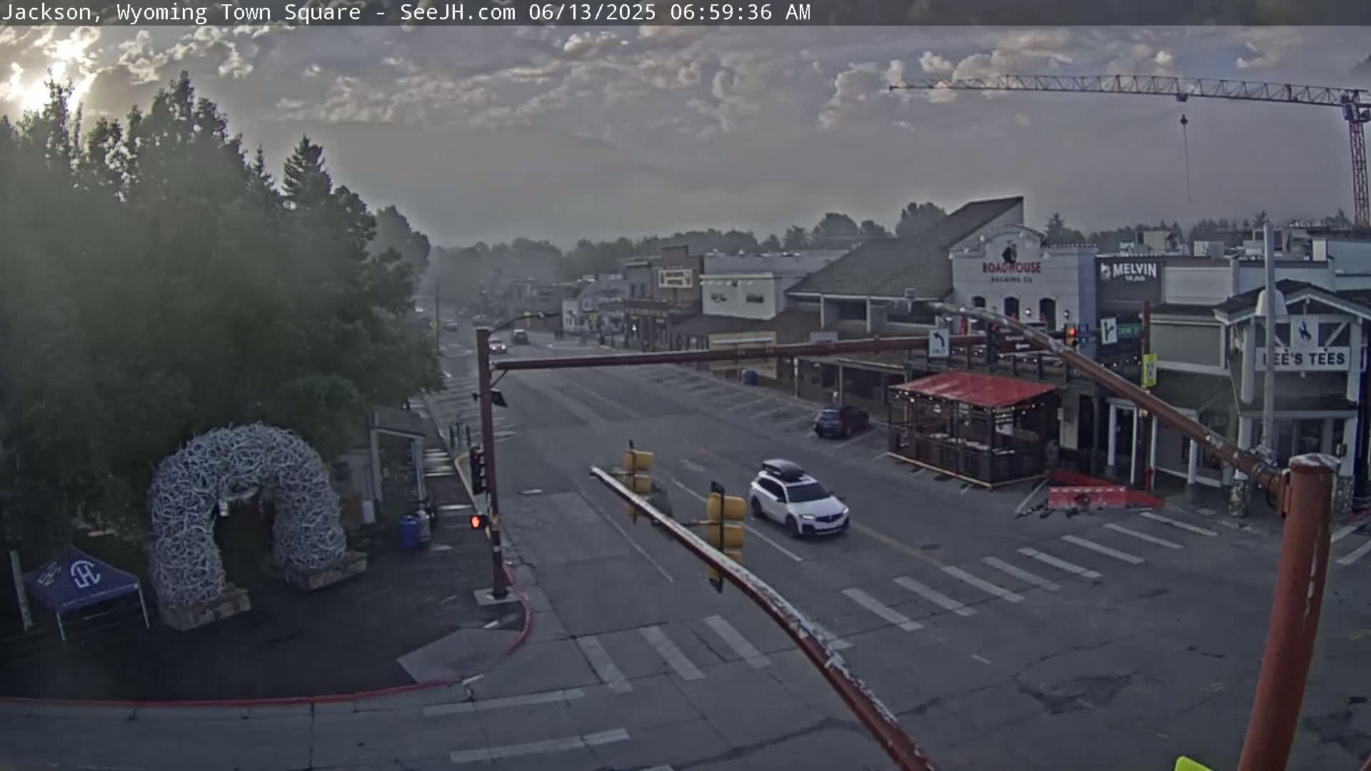 A mostly cloudy sunrise illuminates a town square with several buildings, a roadway, and sparse traffic.