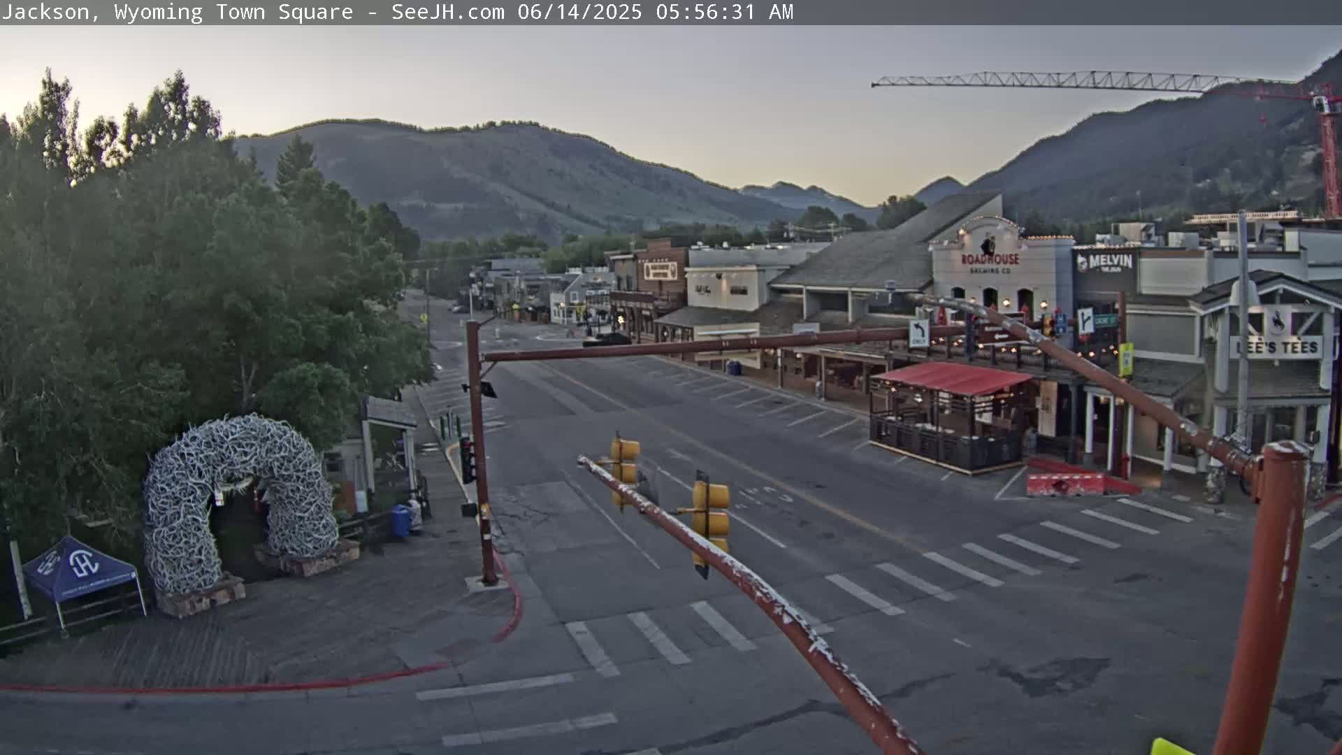 A mostly empty town square, with buildings and a large antler archway visible under a dawn sky.