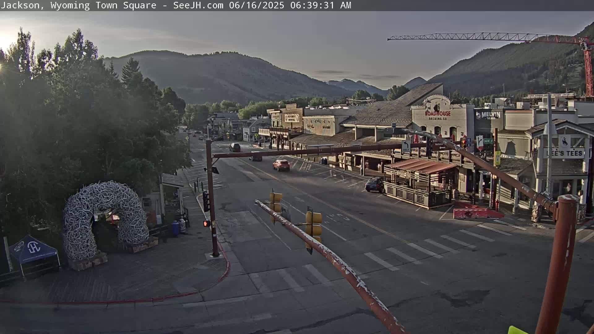 A mostly clear sunrise illuminates a town square with several buildings, a few cars, and a large antler archway.