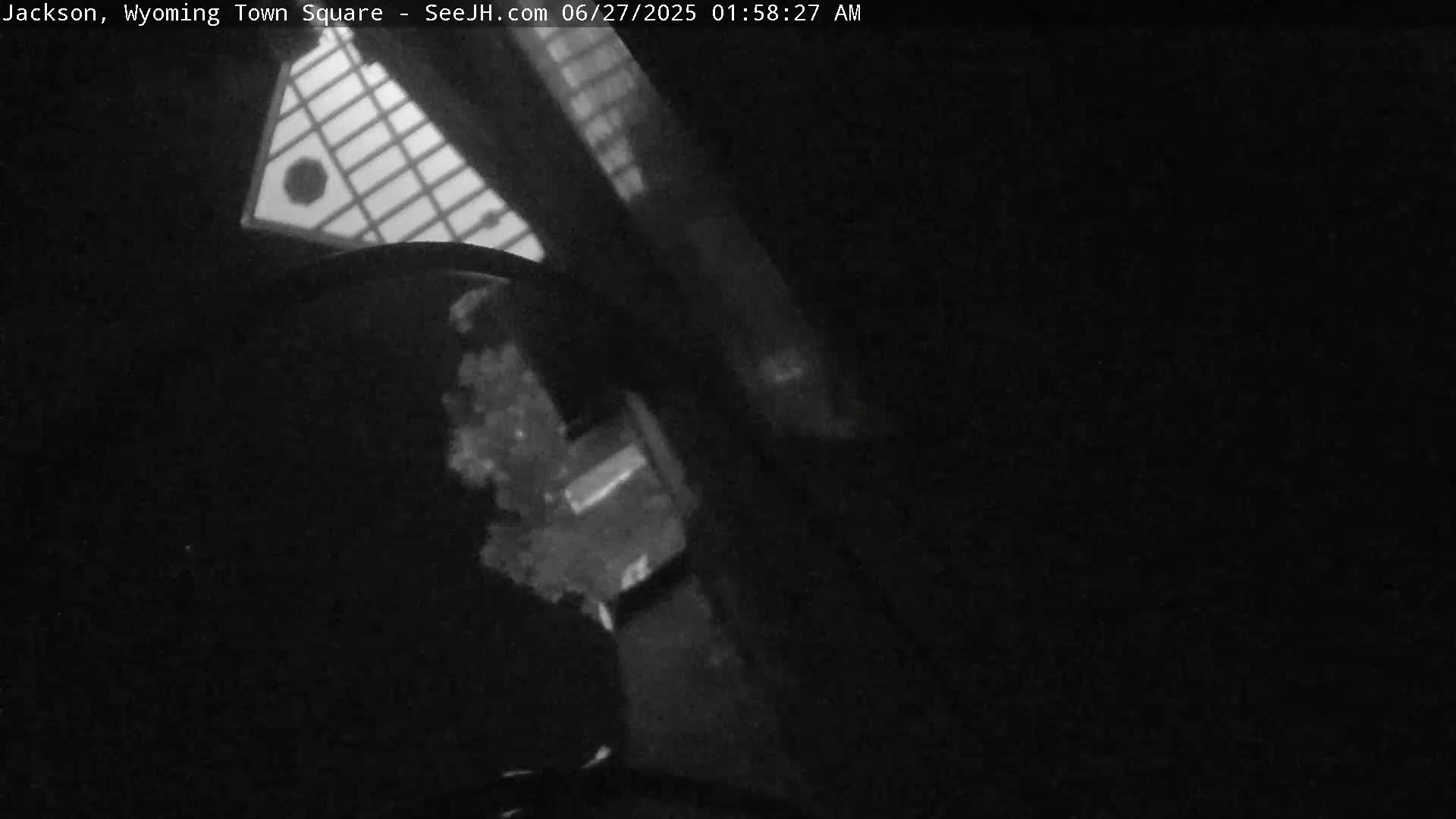A low-light, nighttime image shows a portion of a building's exterior and a small part of what appears to be a street or ground.