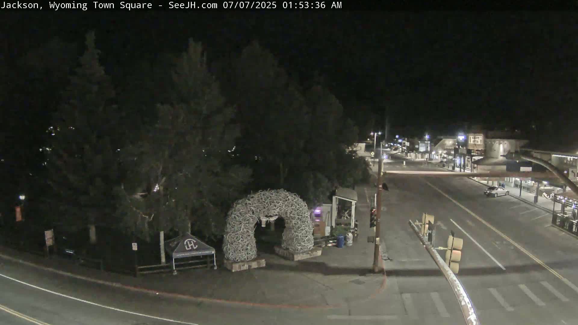 A nighttime view of a town square featuring an antler arch, a mostly empty street, and trees.