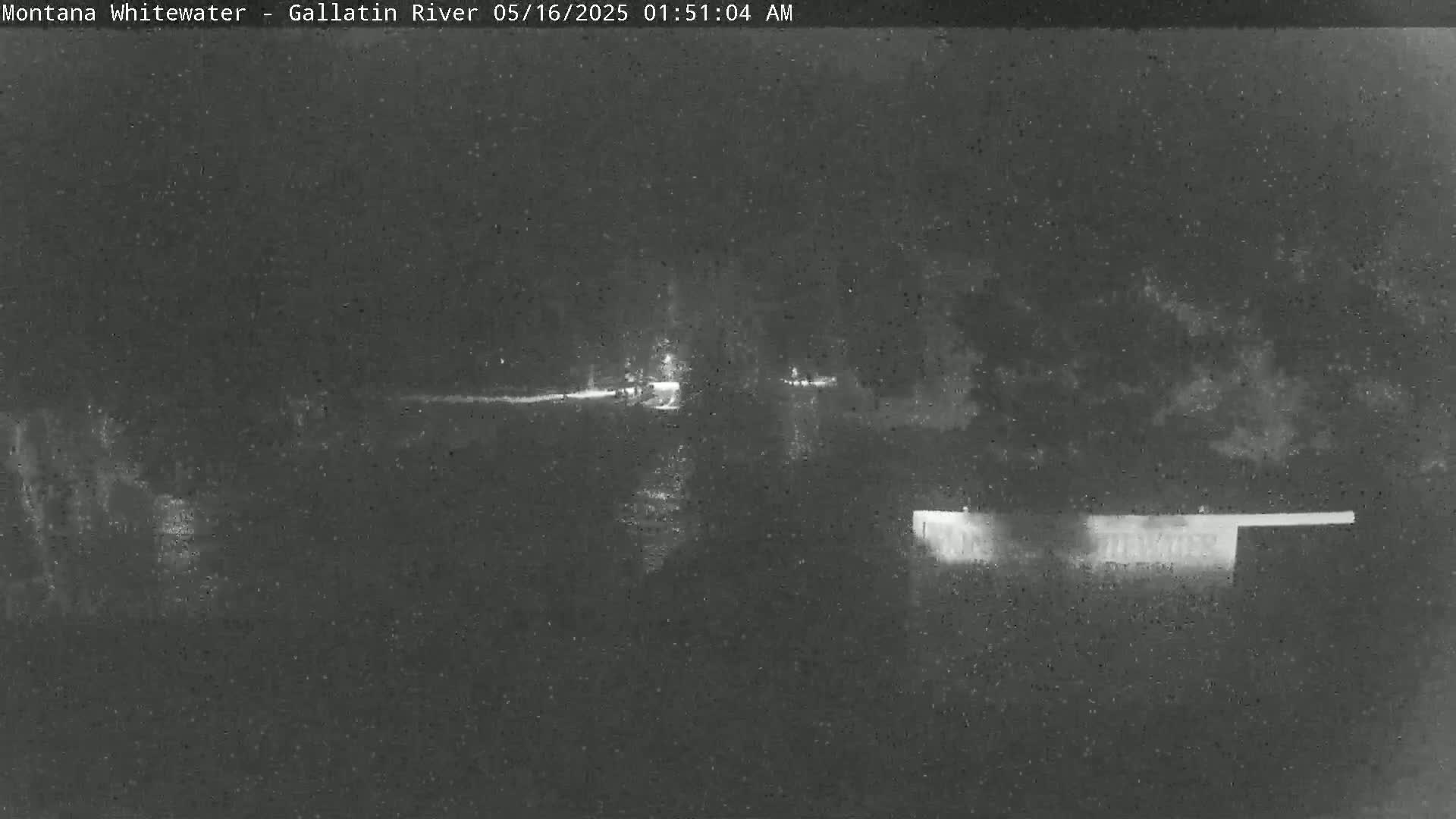 A nighttime, low-light view shows a dark body of water with indistinct shoreline features and some faint lights in the distance.