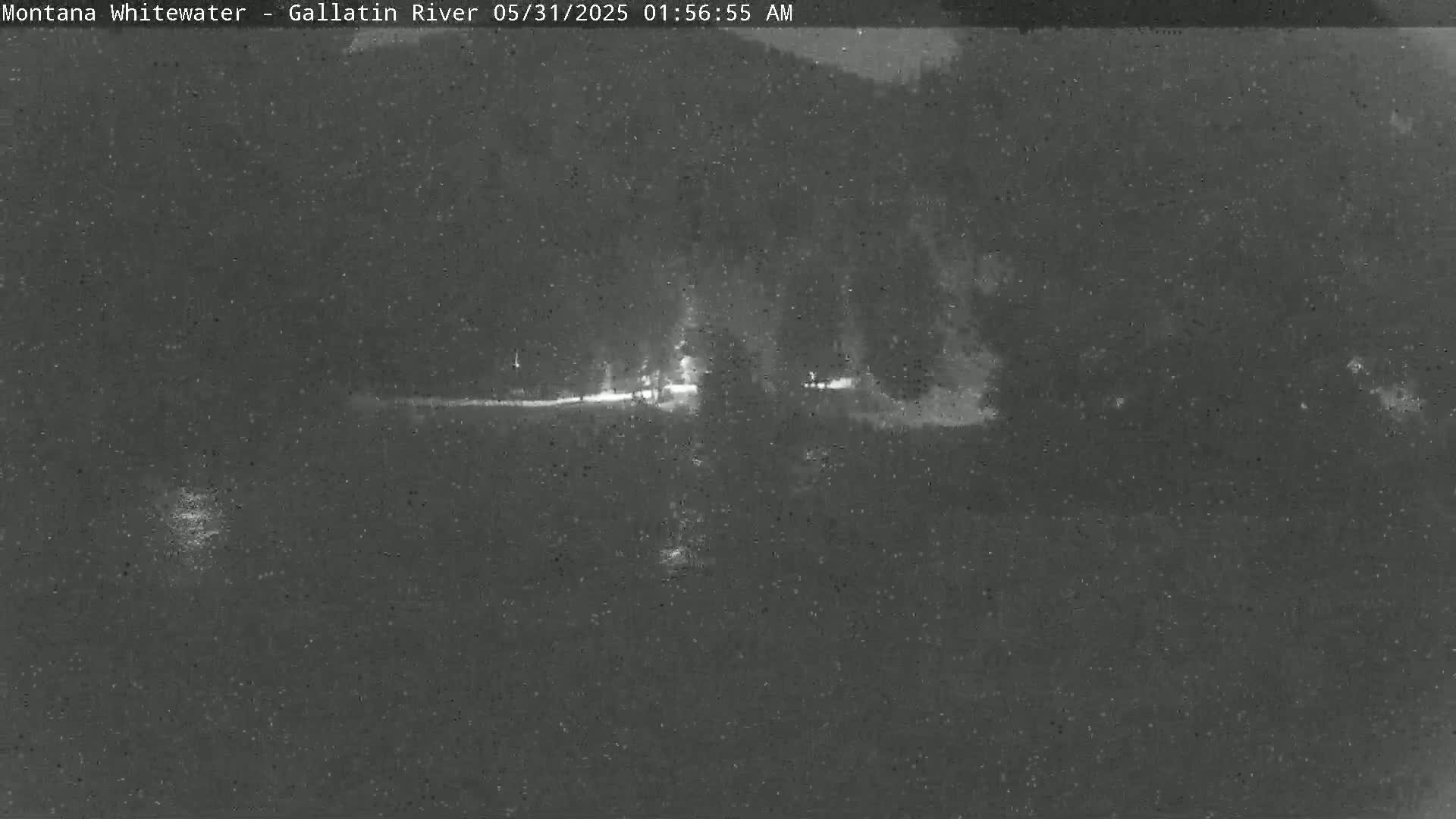 A nighttime, low-light image shows a dark, flat landscape with a faintly visible road and some distant lights.