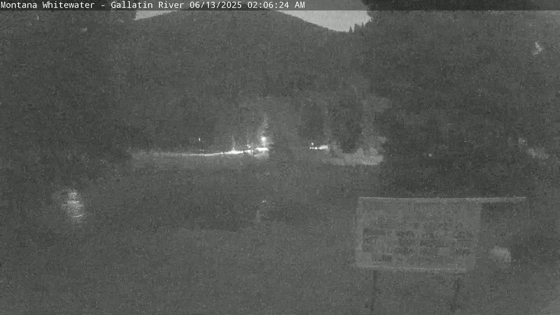 A nighttime, low-light view of a dark body of water, a flat area of land, and dark trees in the background.
