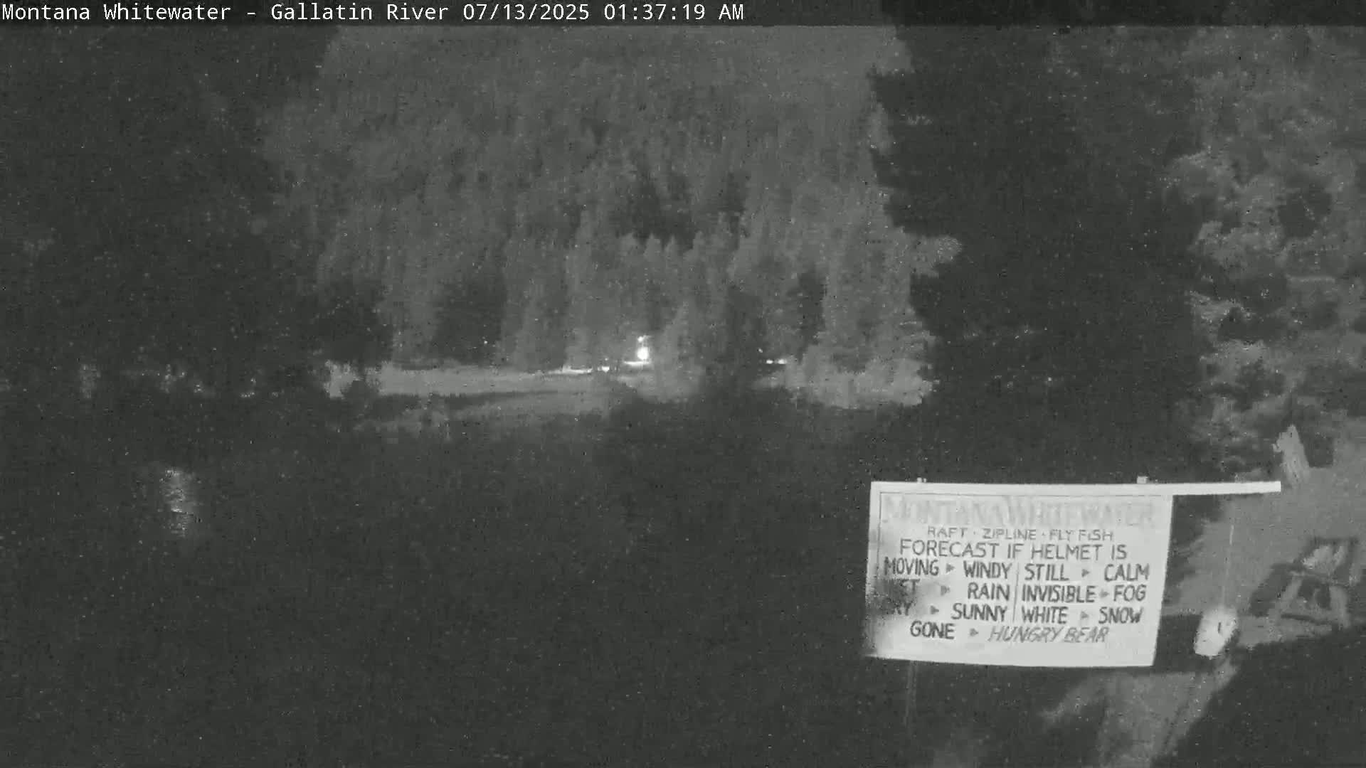 A nighttime, low-light view of a road or path that leads to a dark, wooded area.