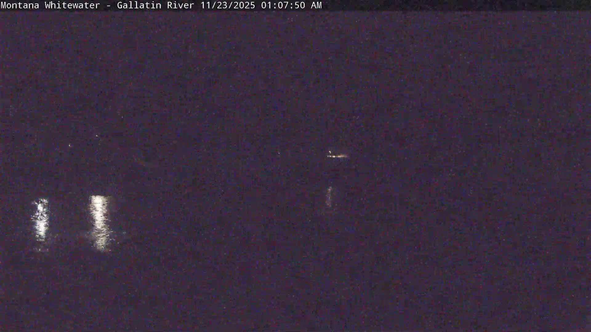 The image displays a very dark outdoor scene at night, featuring several bright reflections on a calm body of water, suggesting clear and calm weather conditions.