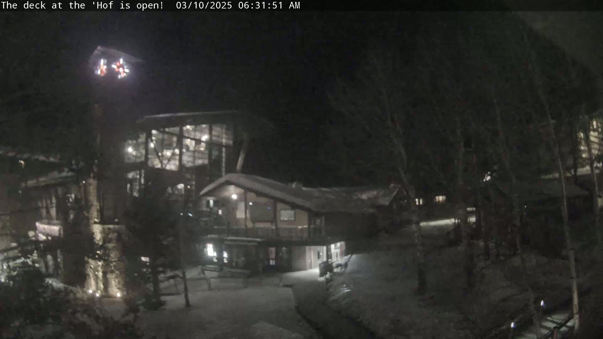 A nighttime view of a snow-covered lodge complex with illuminated windows, surrounded by dark trees.
