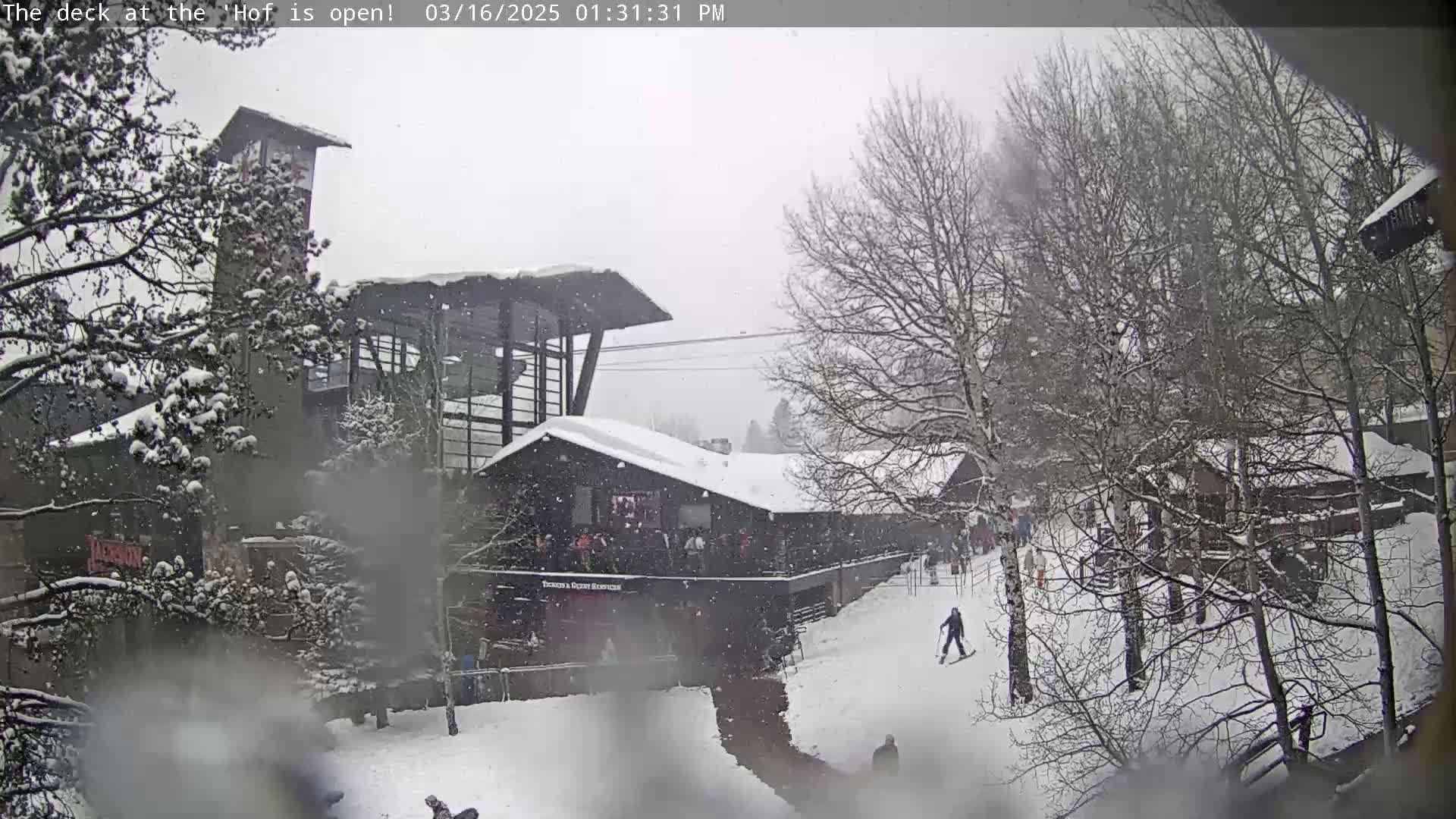 A snow-covered ski lodge and surrounding area with several people skiing and walking in light snowfall.