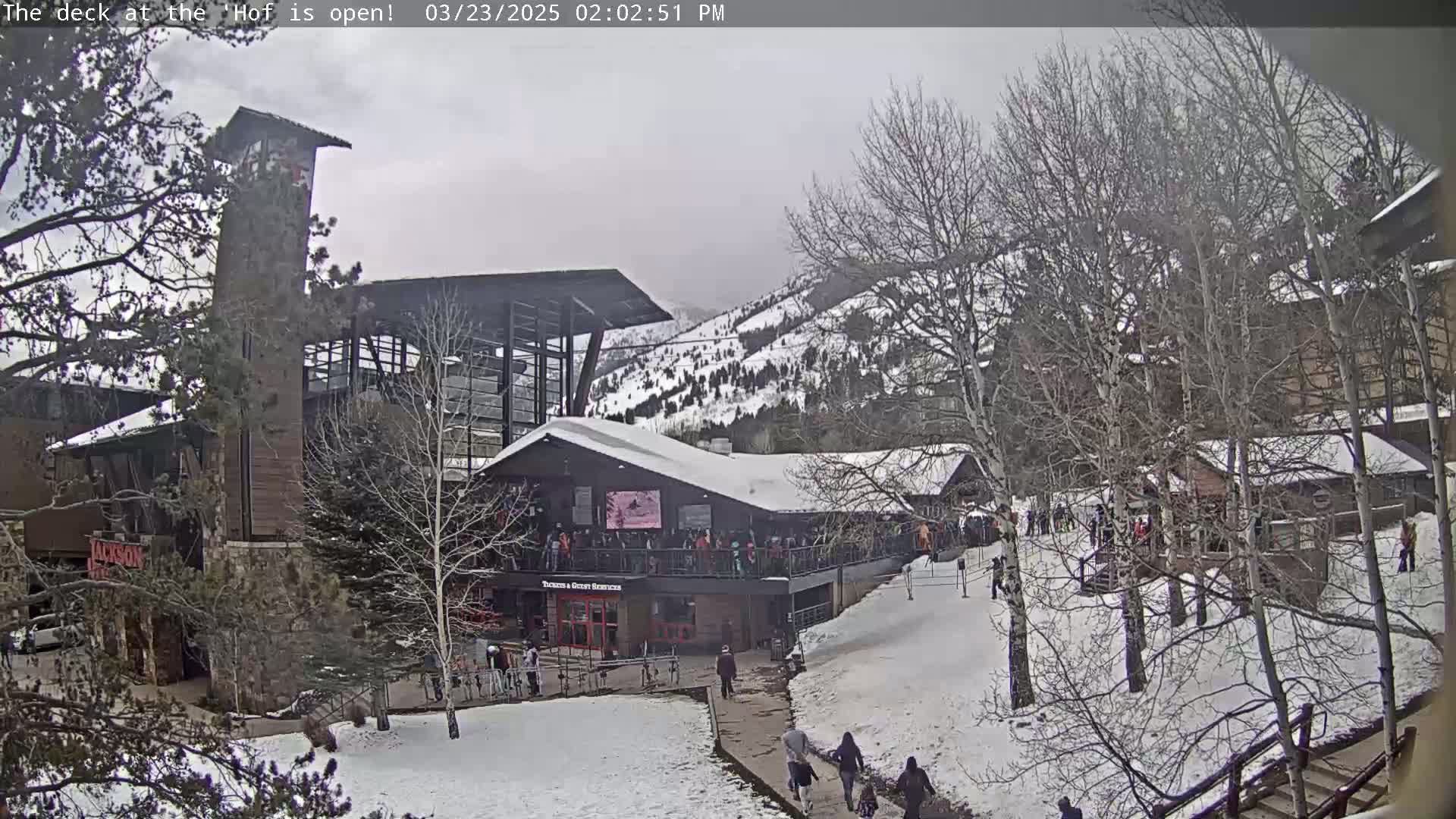 A snow-covered mountain resort, with several buildings and people walking around on a cloudy day.