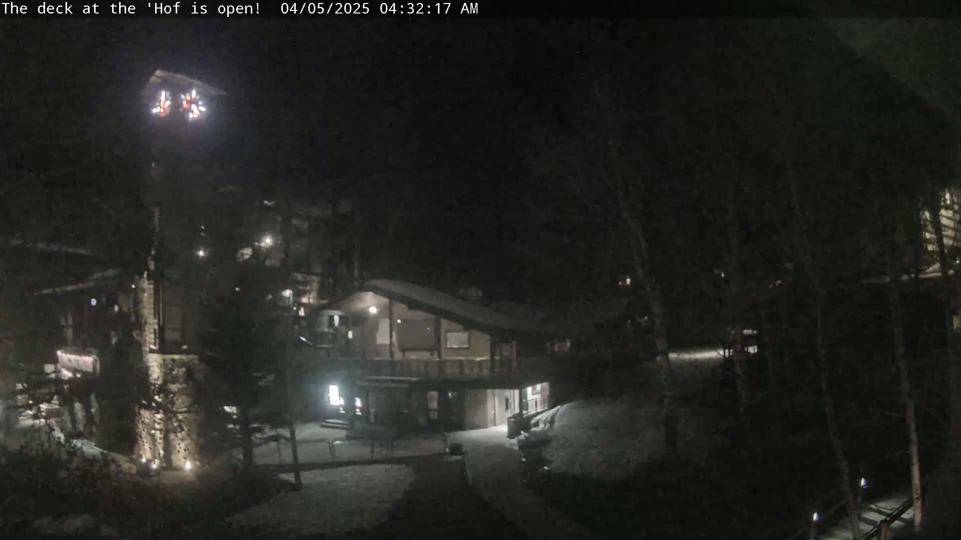 A nighttime view of a snow-covered deck and surrounding buildings, illuminated by artificial lights.