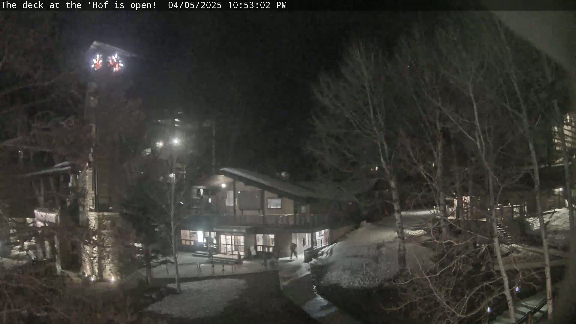 A nighttime view of a snow-covered area with several buildings, some trees, and a small group of people near a building.