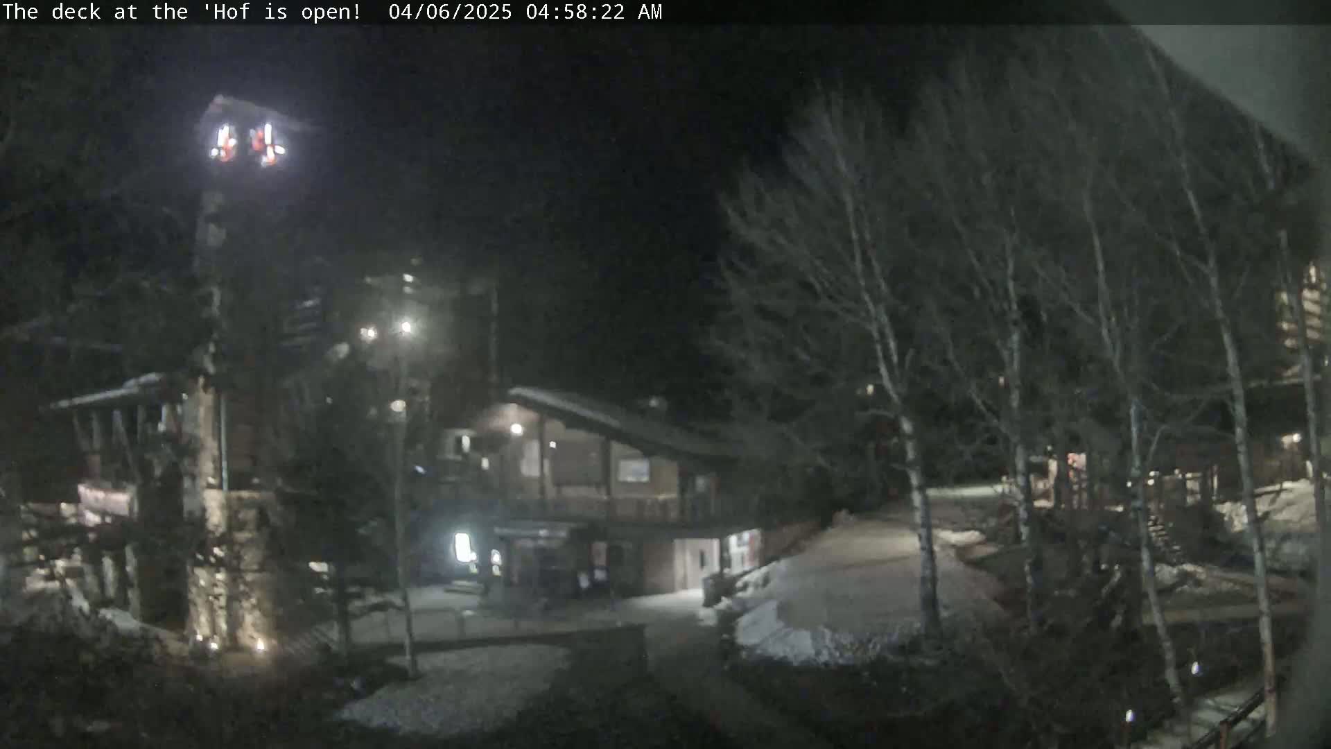 A nighttime view of a snow-dusted outdoor area with buildings and bare trees under a dark sky.