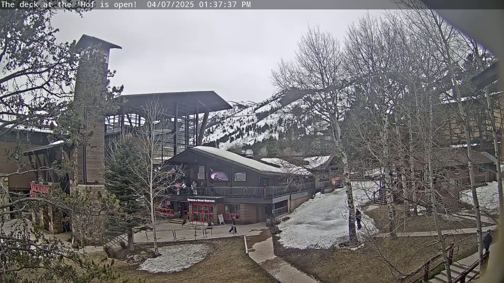 A snow-dusted outdoor scene shows a multi-story building complex with a deck, walkways, and bare trees under an overcast sky.
