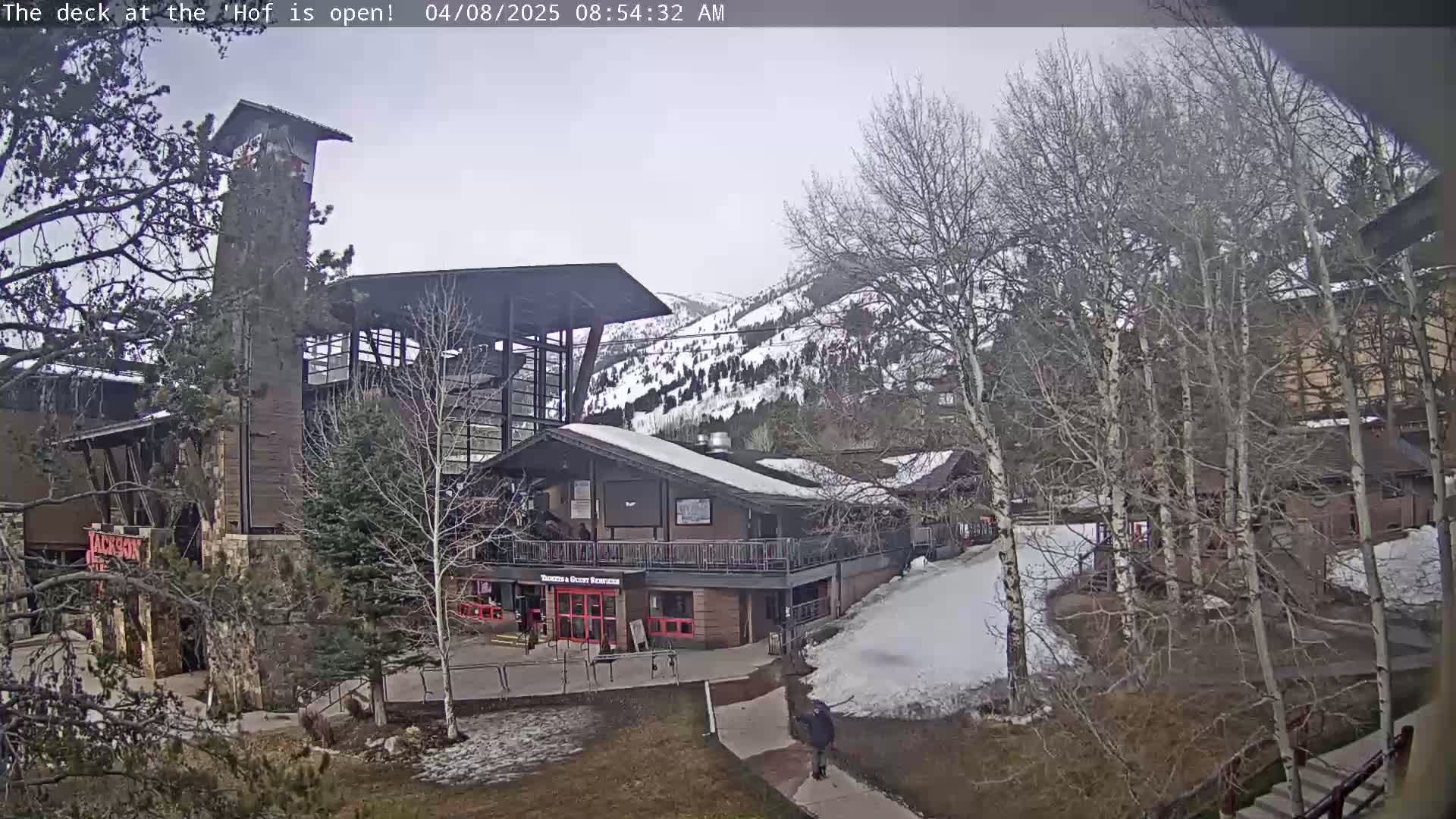 A person walks past a building complex nestled in a snowy mountainside on an overcast day.