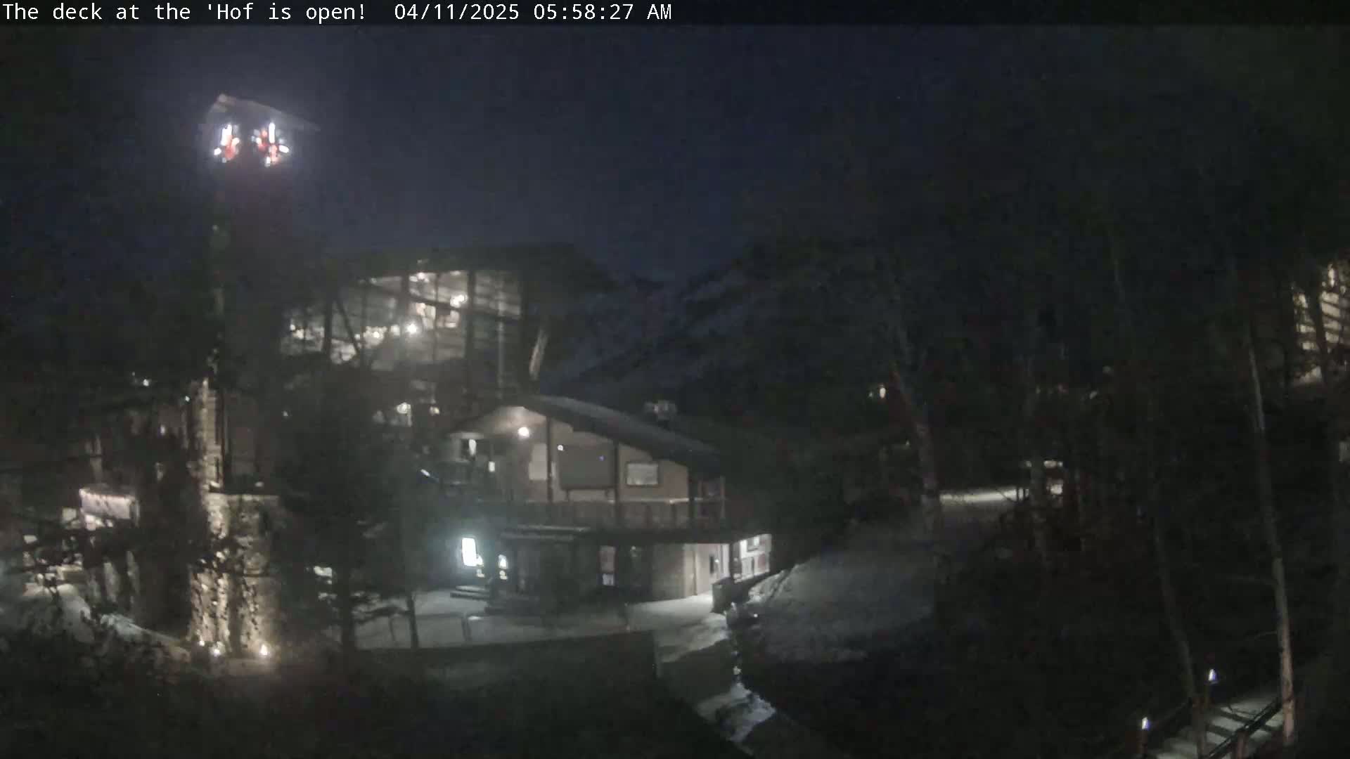 A nighttime view of a lit-up building complex nestled in a dark, wooded area under a clear, dark sky.