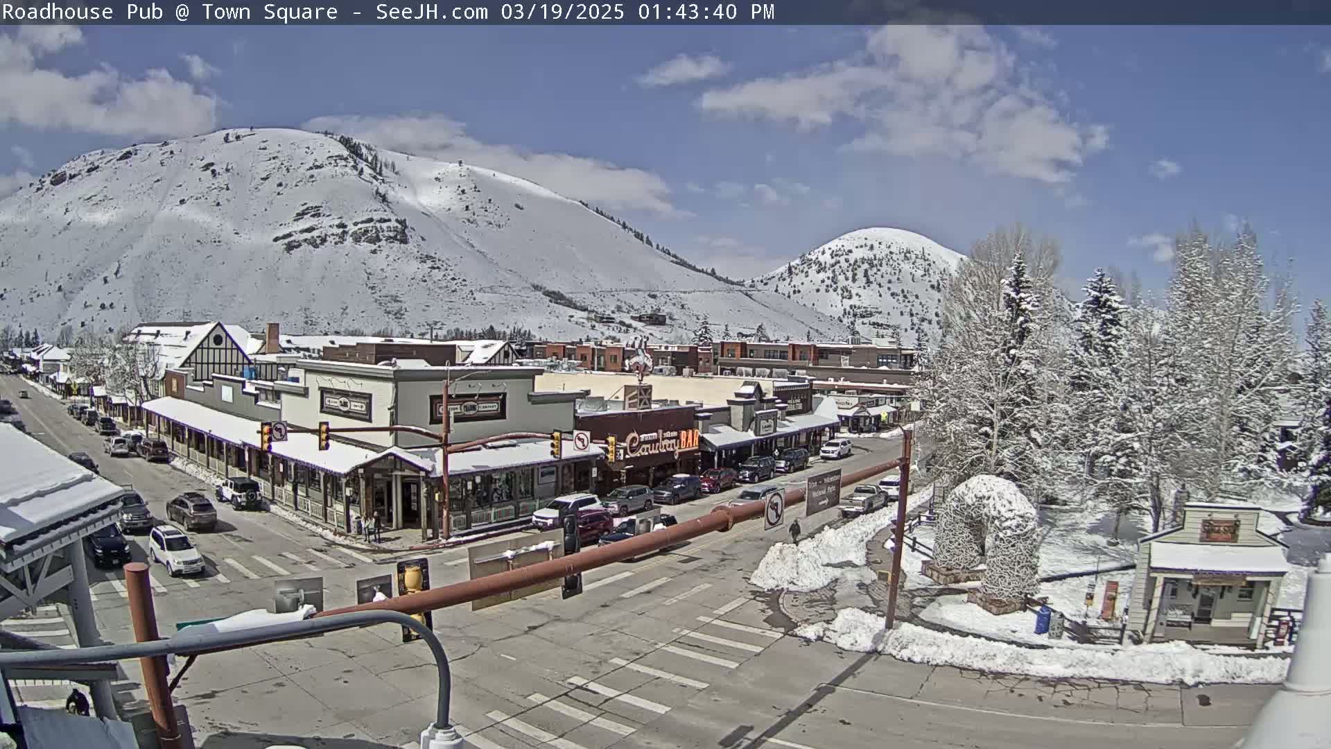 A snow-dusted town nestled in a valley between snow-capped mountains under a partly sunny sky.