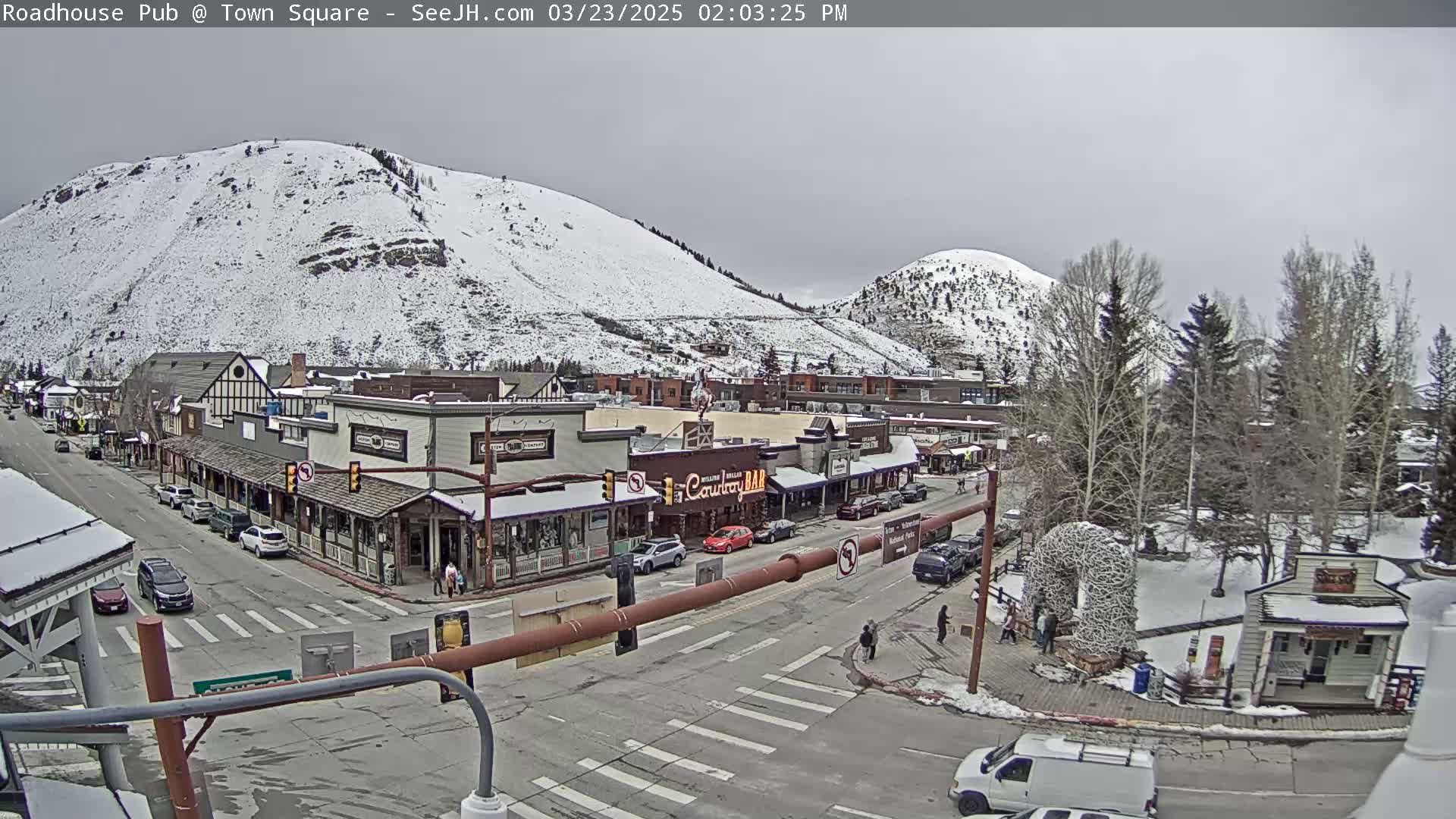 A snow-dusted town with buildings lining a street, situated at the base of snow-covered mountains under an overcast sky.
