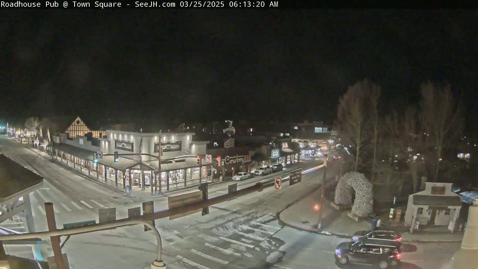 A snow-covered town square at night, with several cars and buildings visible under dark skies.