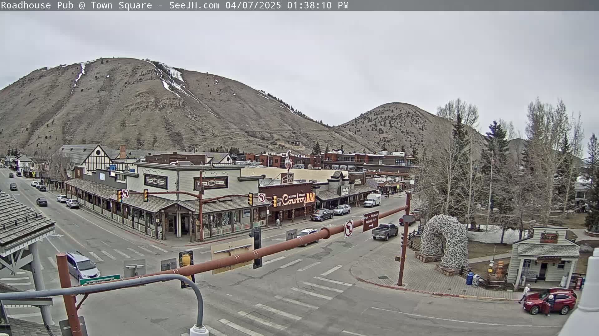 A town square nestled between mountains on an overcast day, with cars on the streets and buildings lining the square.